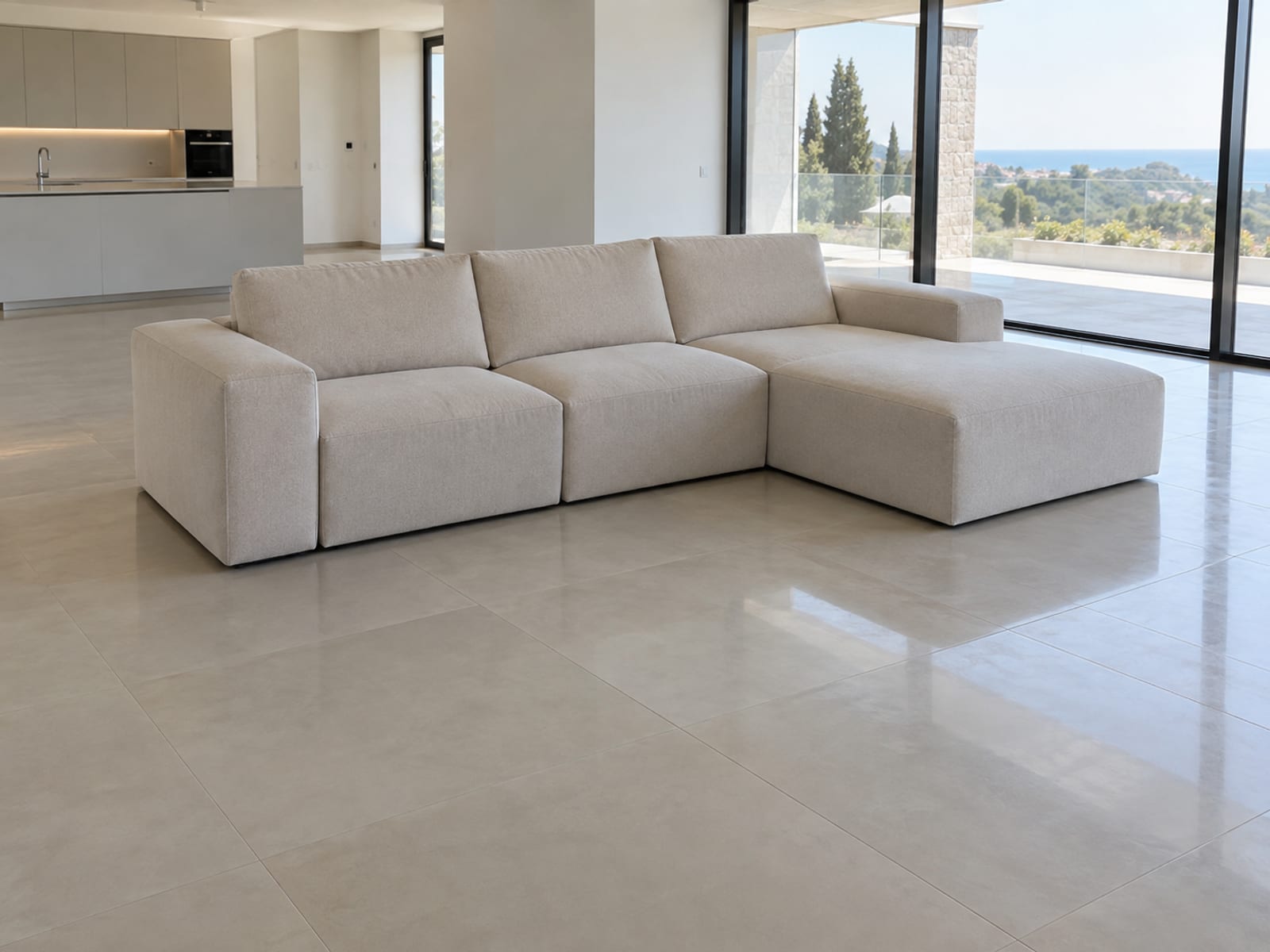 A modular sofa of square seat blocks standing directly on large smooth pale porcelain floor tiles in a daylit open-plan room with no rug, photographed from standing height at a three-quarter angle so the smooth, faintly reflective floor under and around the whole sofa reads as the surface it has to hold its place on