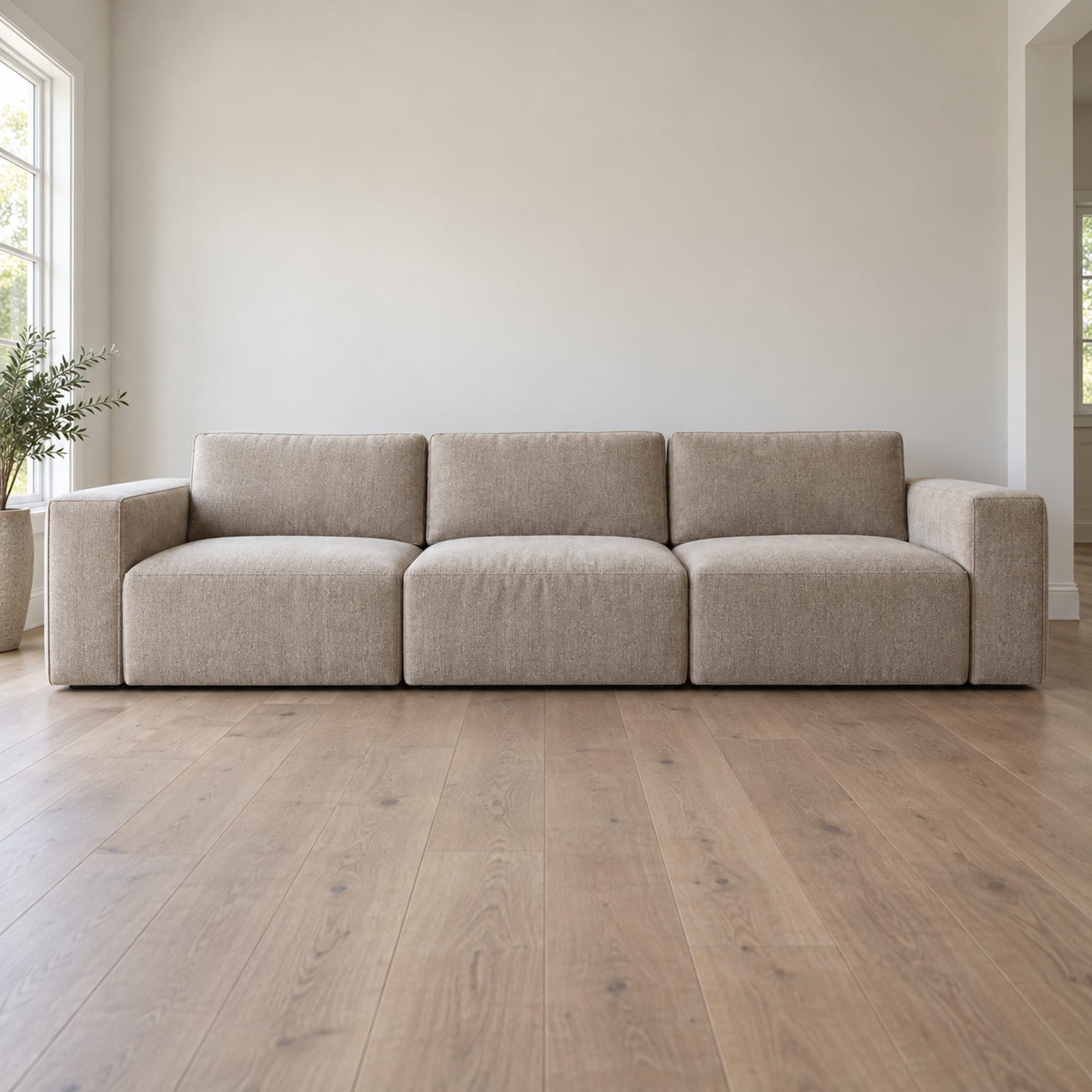 A low modular sofa of three square seat blocks with separate plain upholstered back and arm pieces in a dense warm putty chenille, standing against a plain wall, photographed square on from the front at a very low height just above the floorboards
