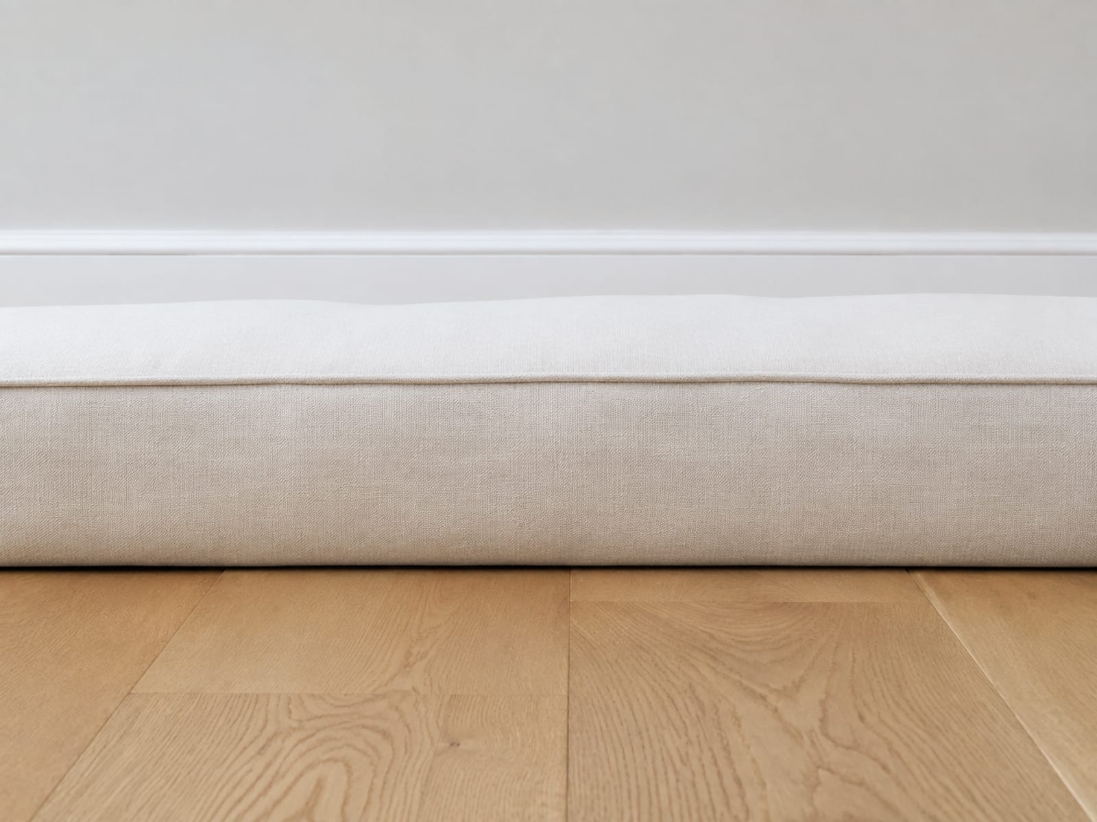 The seat of an upholstered sofa seen square from the side at floor level, its flat top surface running across the picture against the fixed line of the wall baseboard
