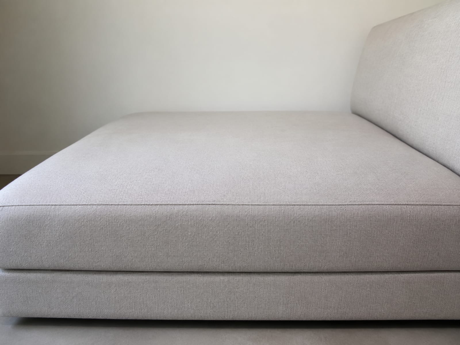A very deep sofa seat seen square from the side at seat level against a plain wall, the long reach from the front edge back to the base of the back cushion filling the frame