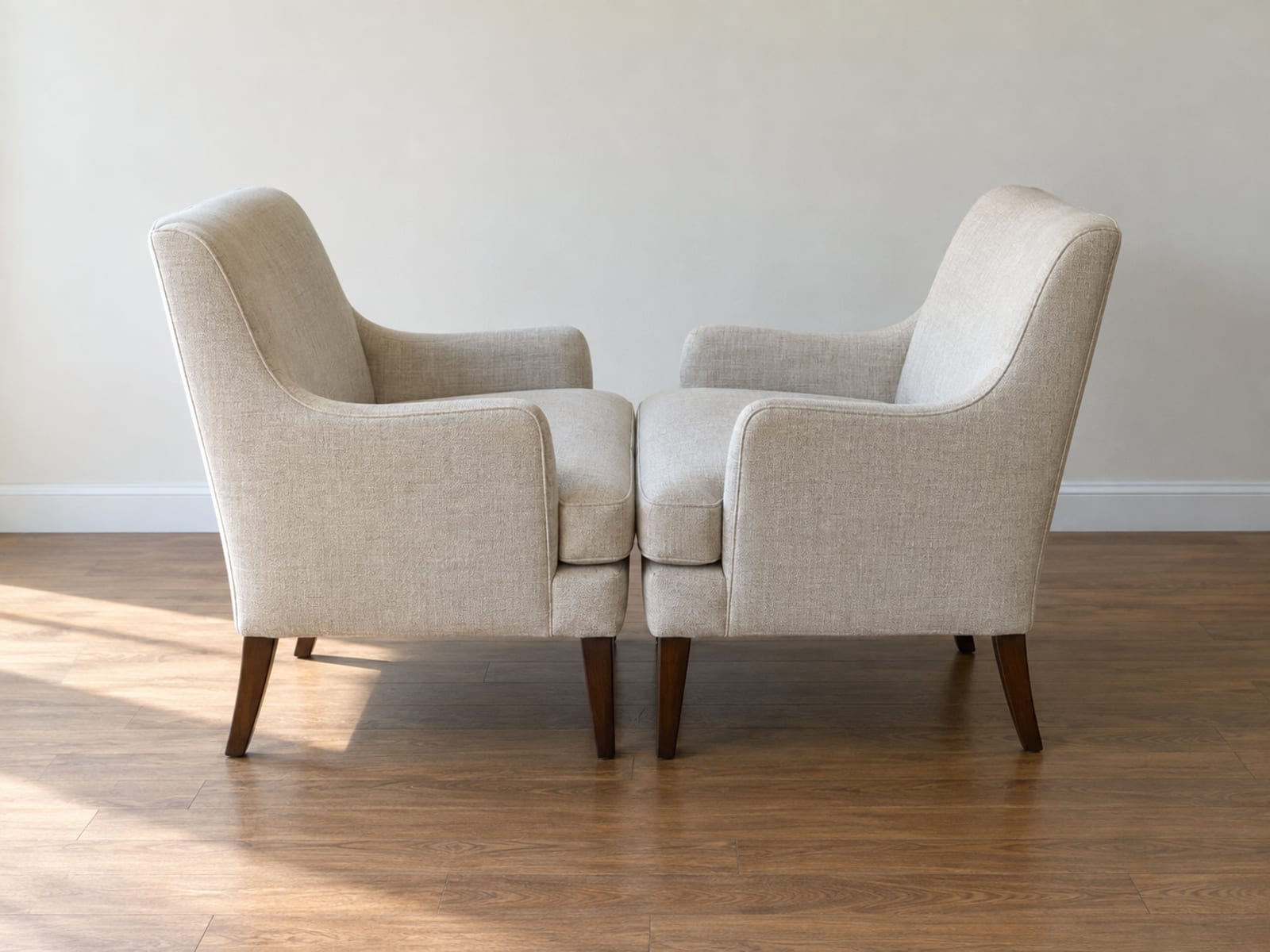 Two matching upholstered armchairs pushed together seat edge to seat edge so they face each other and form one short enclosed surface between their arms, standing in an empty daylit room and photographed from a raised side angle at standing height