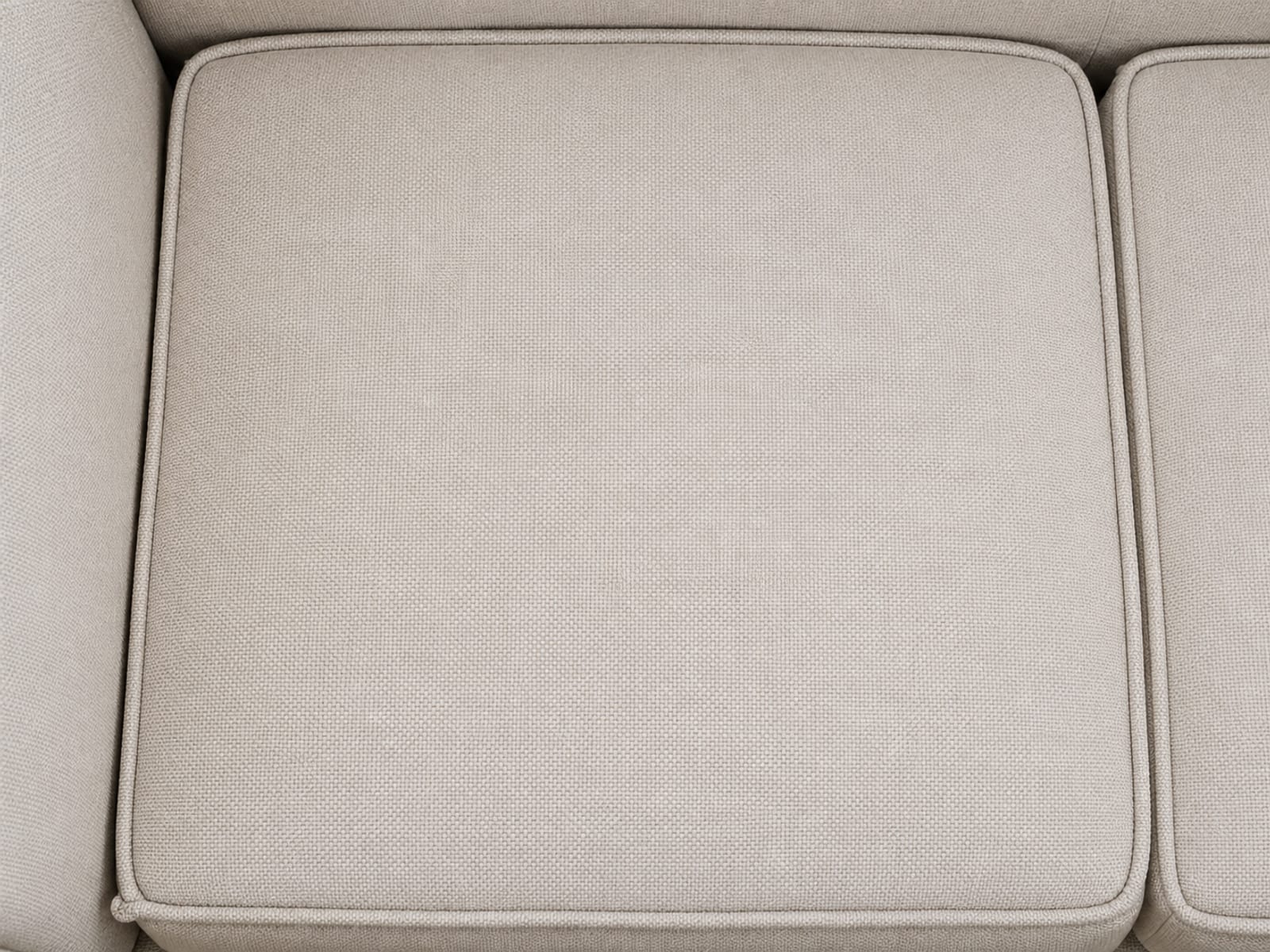 A single pale woven seat cushion seen square from above, its corded piping running around all four sides so the whole face reads as one bounded panel