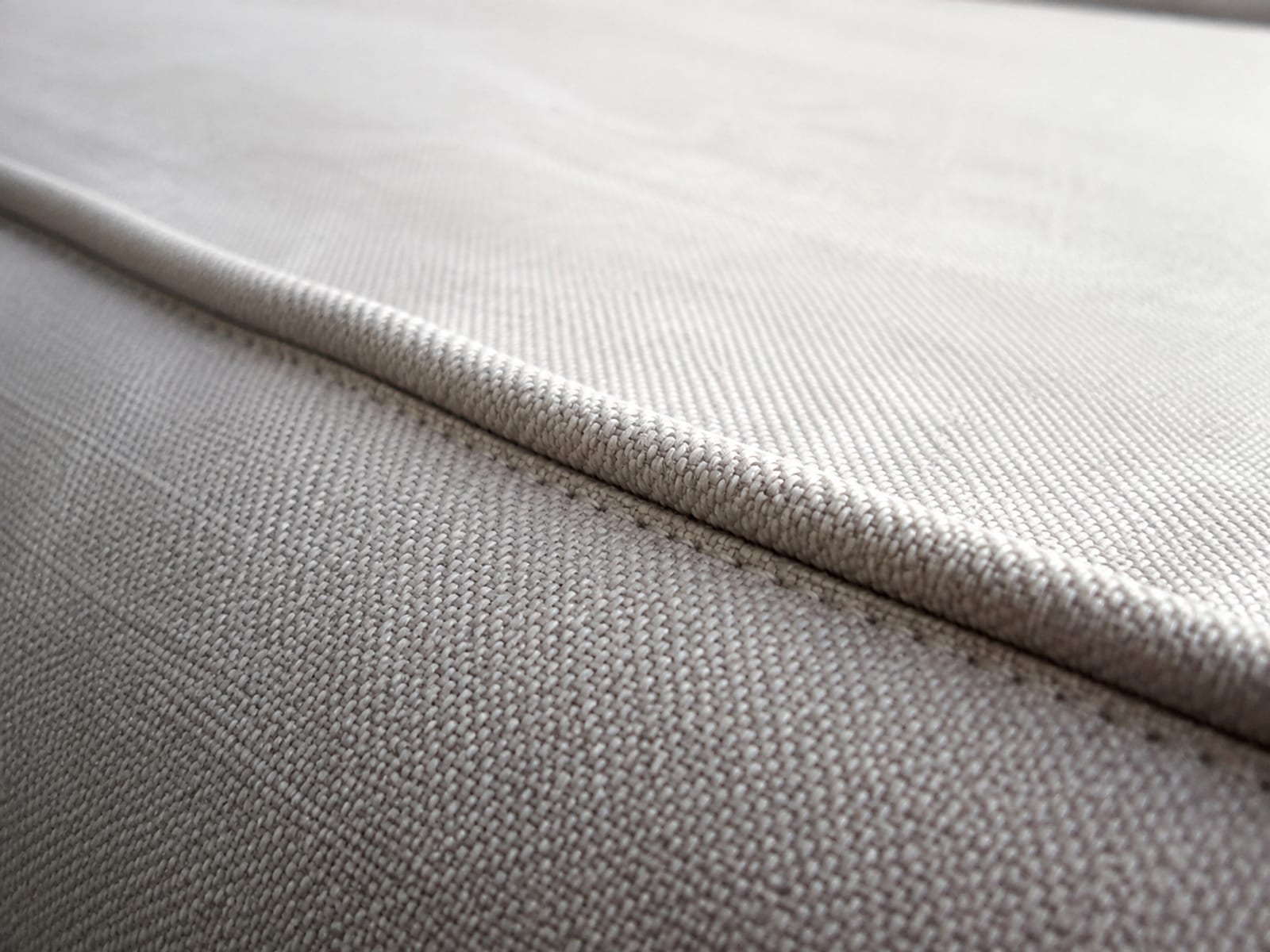 A raking close view along the corded piping where a seat cushion meets the seat platform, the welt running as a raised line with clean fabric rising either side