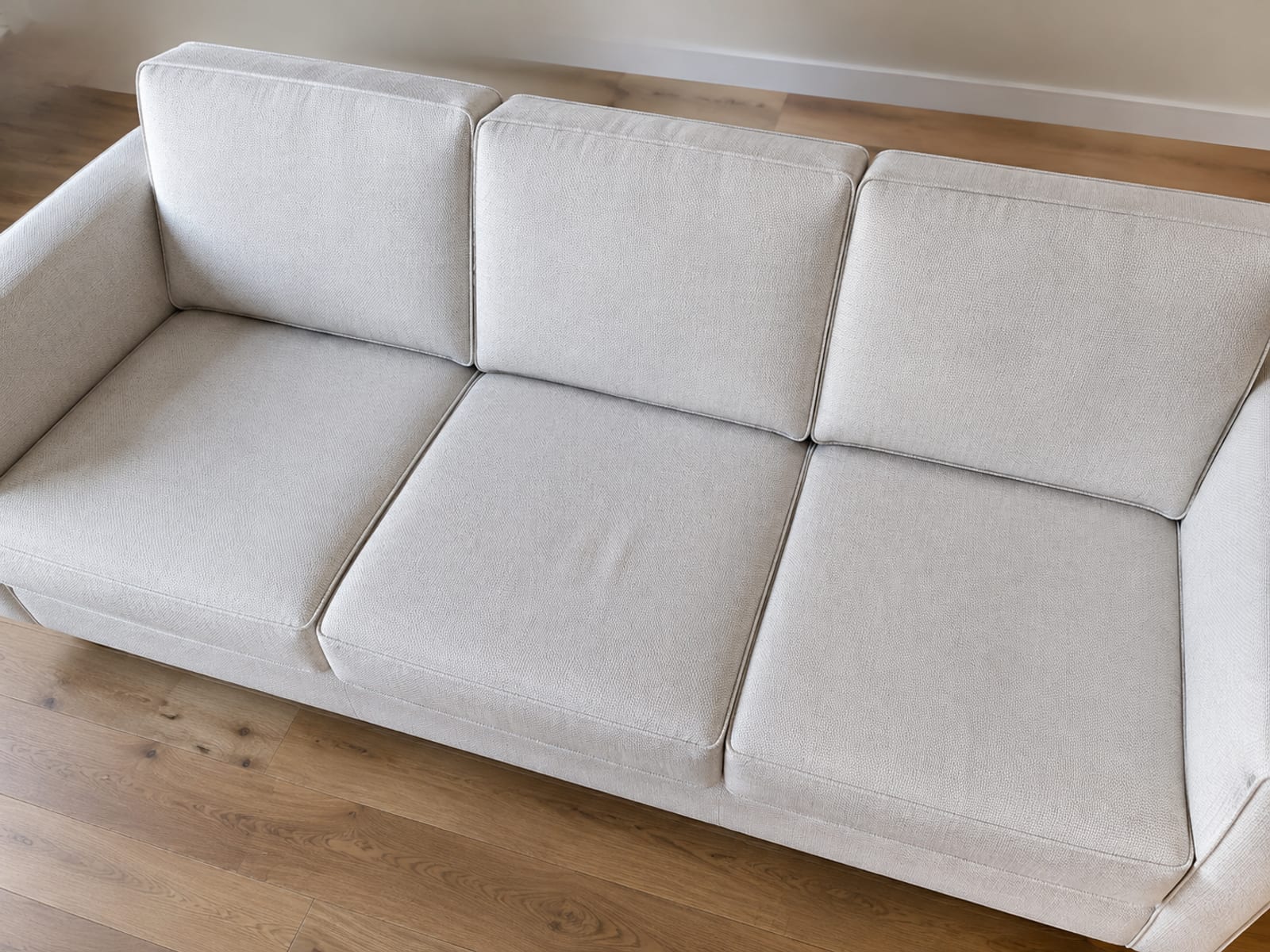 A high view across the whole seating surface of a pale three-seat sofa, the piping dividing it into six separate bounded panels