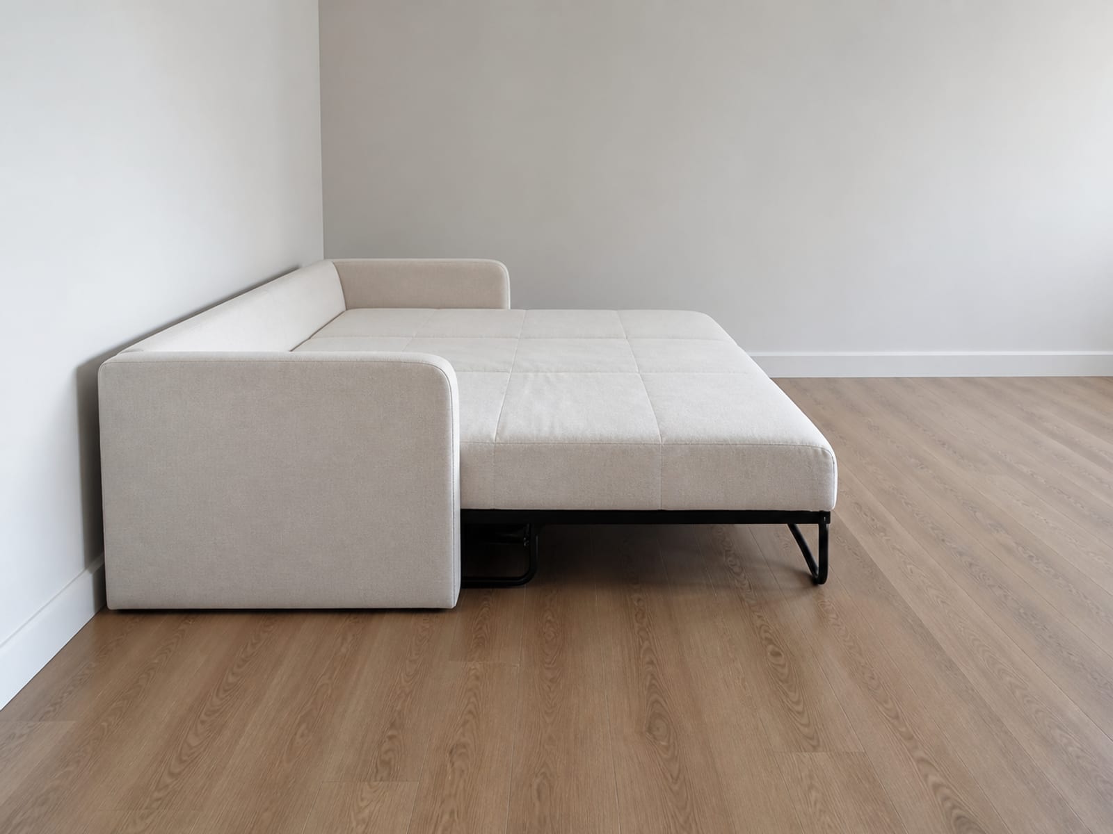 A convertible sofa with its back almost touching a plain wall and its seat travelled forward into the room in the open position, seen square from the side at low height