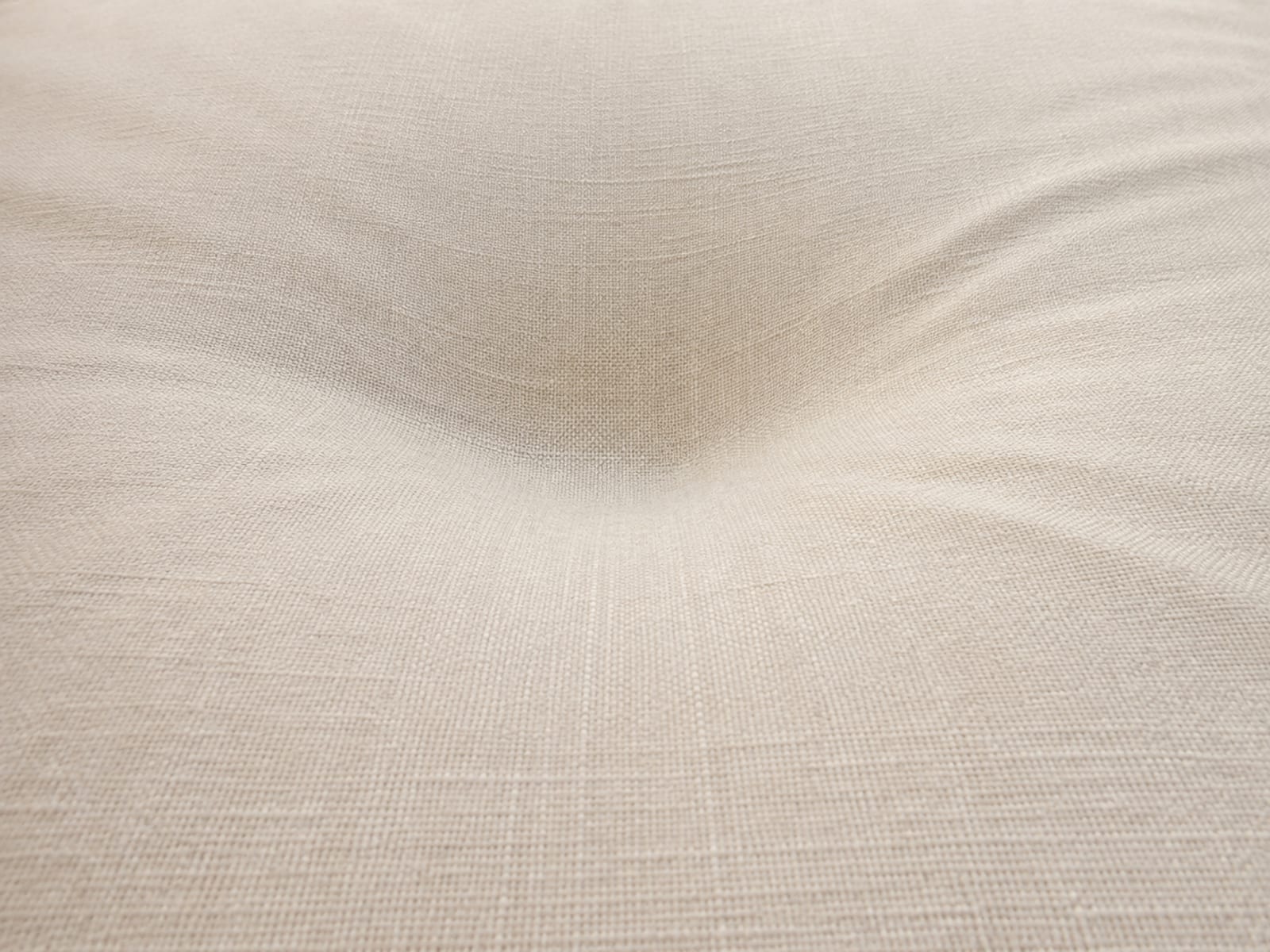 A close raking view across the surface of a plain futon pad lying flat, with a gentle compression hollow showing where somebody habitually sits