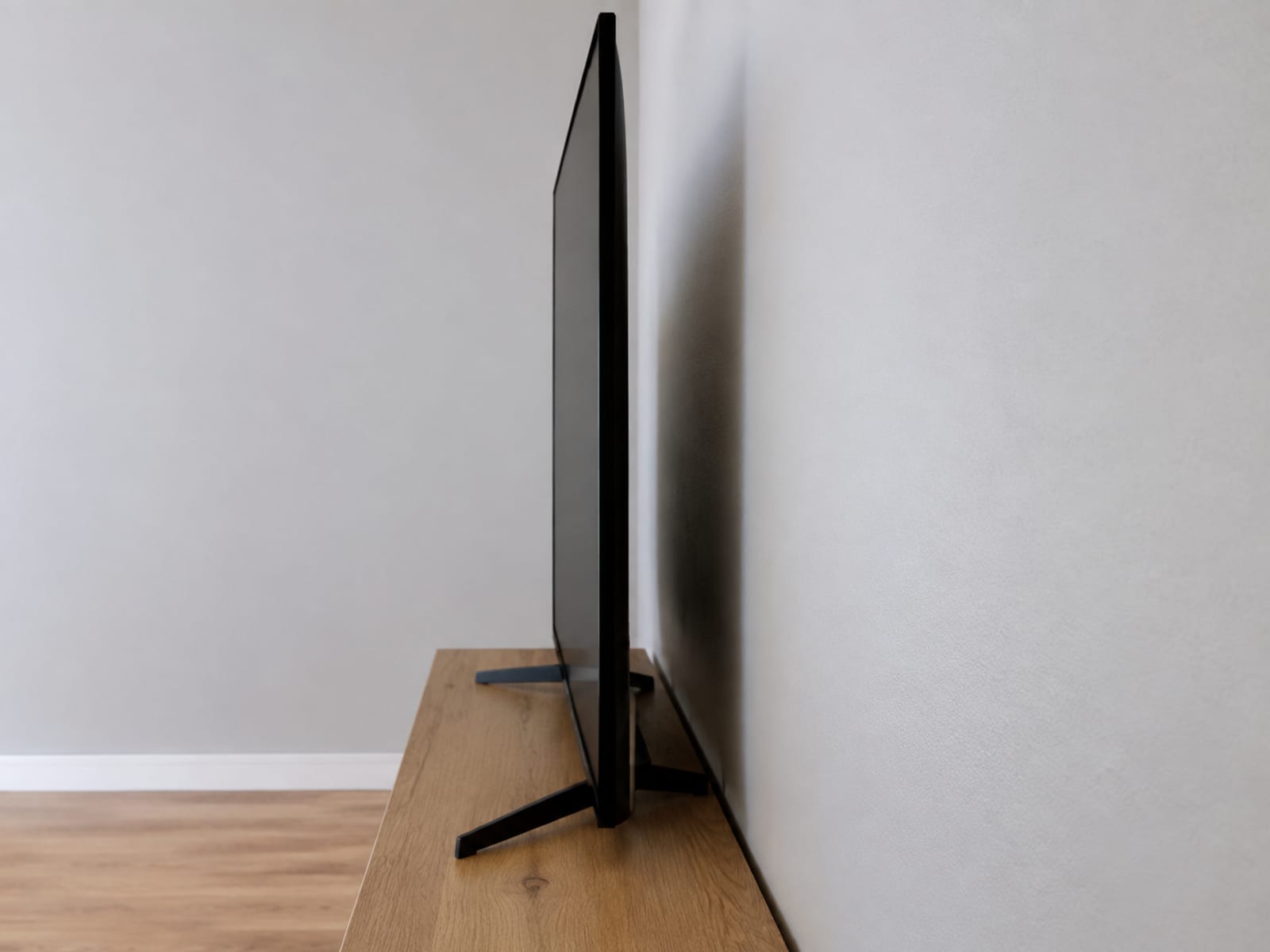 A close side-on view of a flat-panel television standing on a low console against a wall, the depth of the console and the front face of the dark screen in one profile