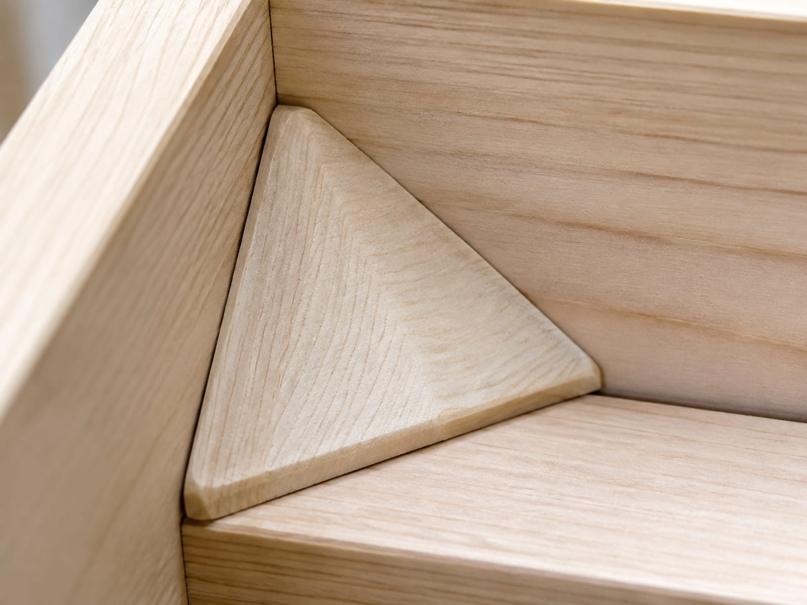 An extremely close view of the inside corner of a bare sofa frame, a triangular timber corner block seated tightly where the side rail meets the front rail