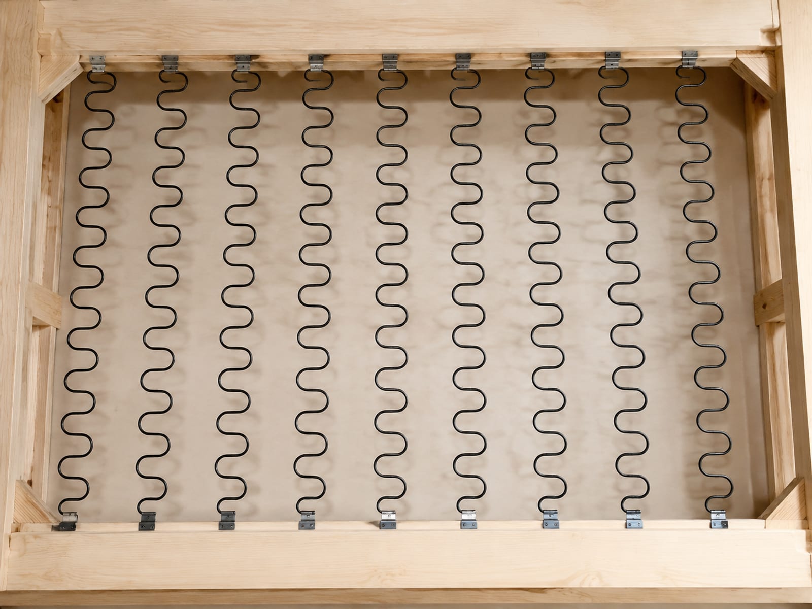 A view down into the open seat of a sofa with the cushions and deck fabric absent, S-curved steel springs stretched front to back across the frame rails