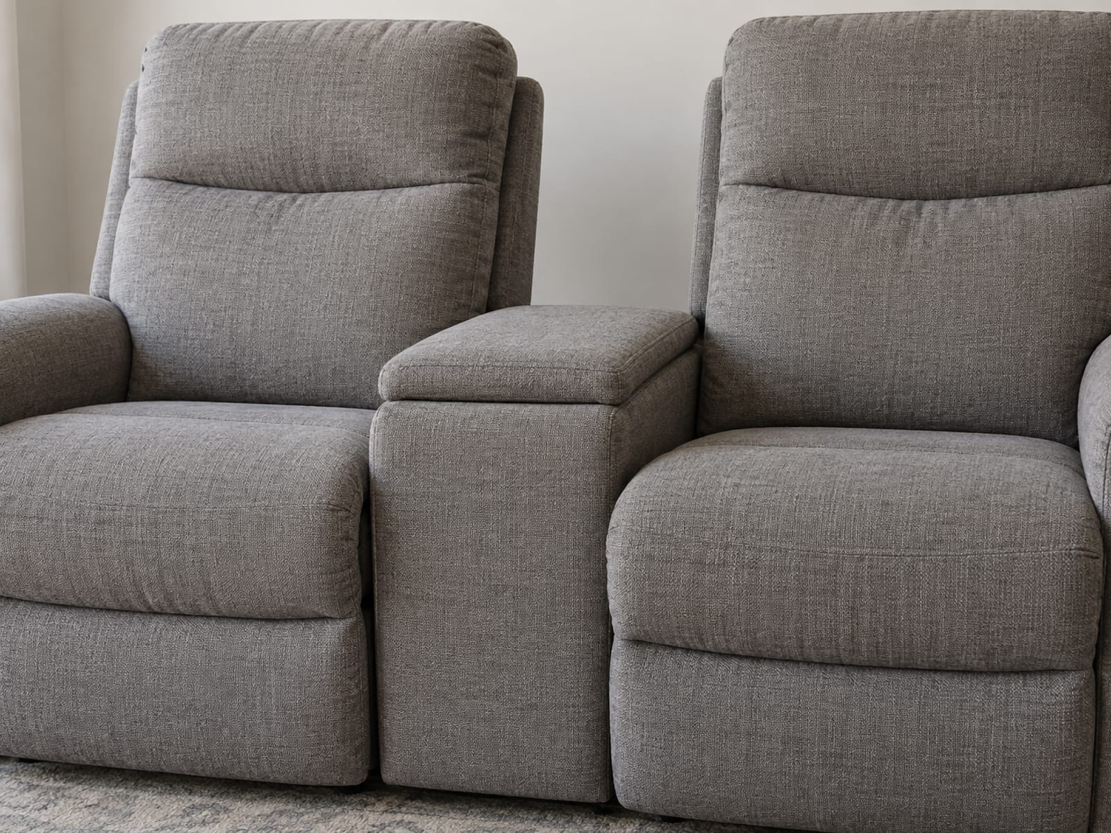 A close front three-quarter view at seat height of two closed, upright reclining seats of a sectional with an upholstered console standing between them, its padded lid closed flat and level with the arms on either side
