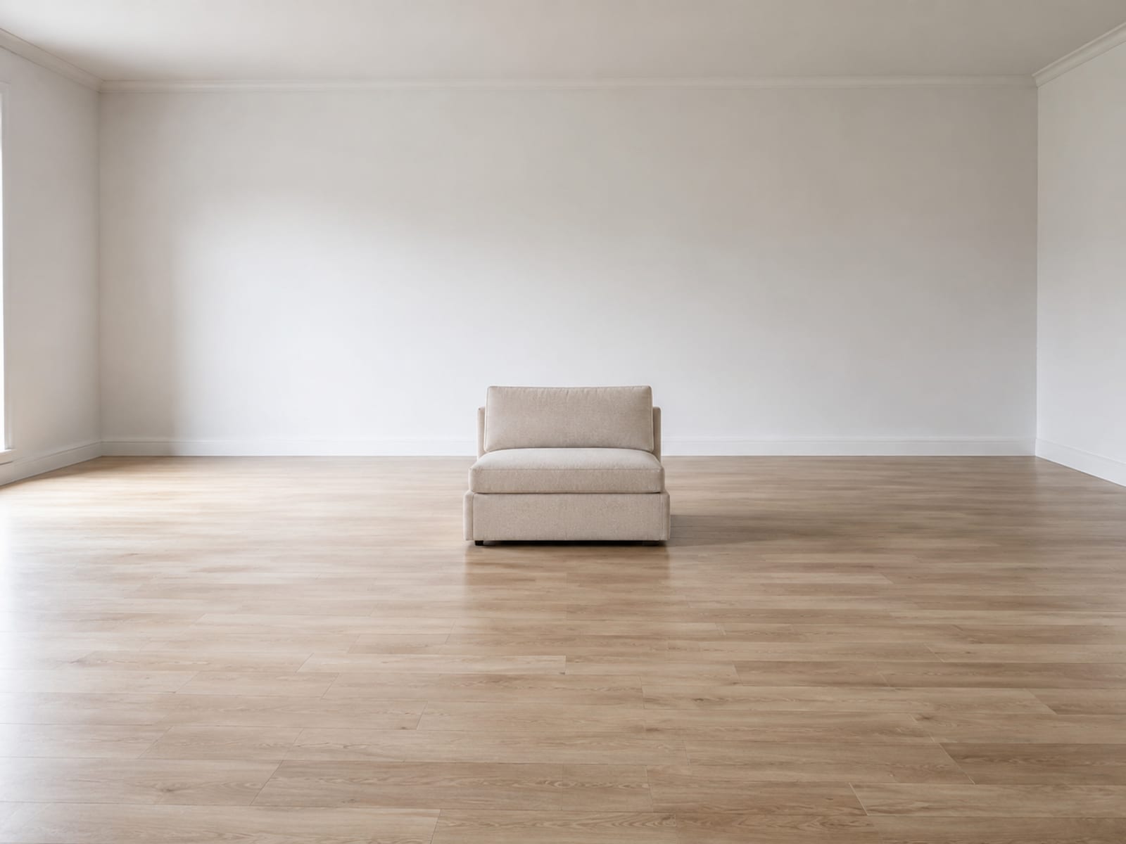 A single one-seat convertible sofa alone in the middle of a large bare room, small against the floor running away on every side of it