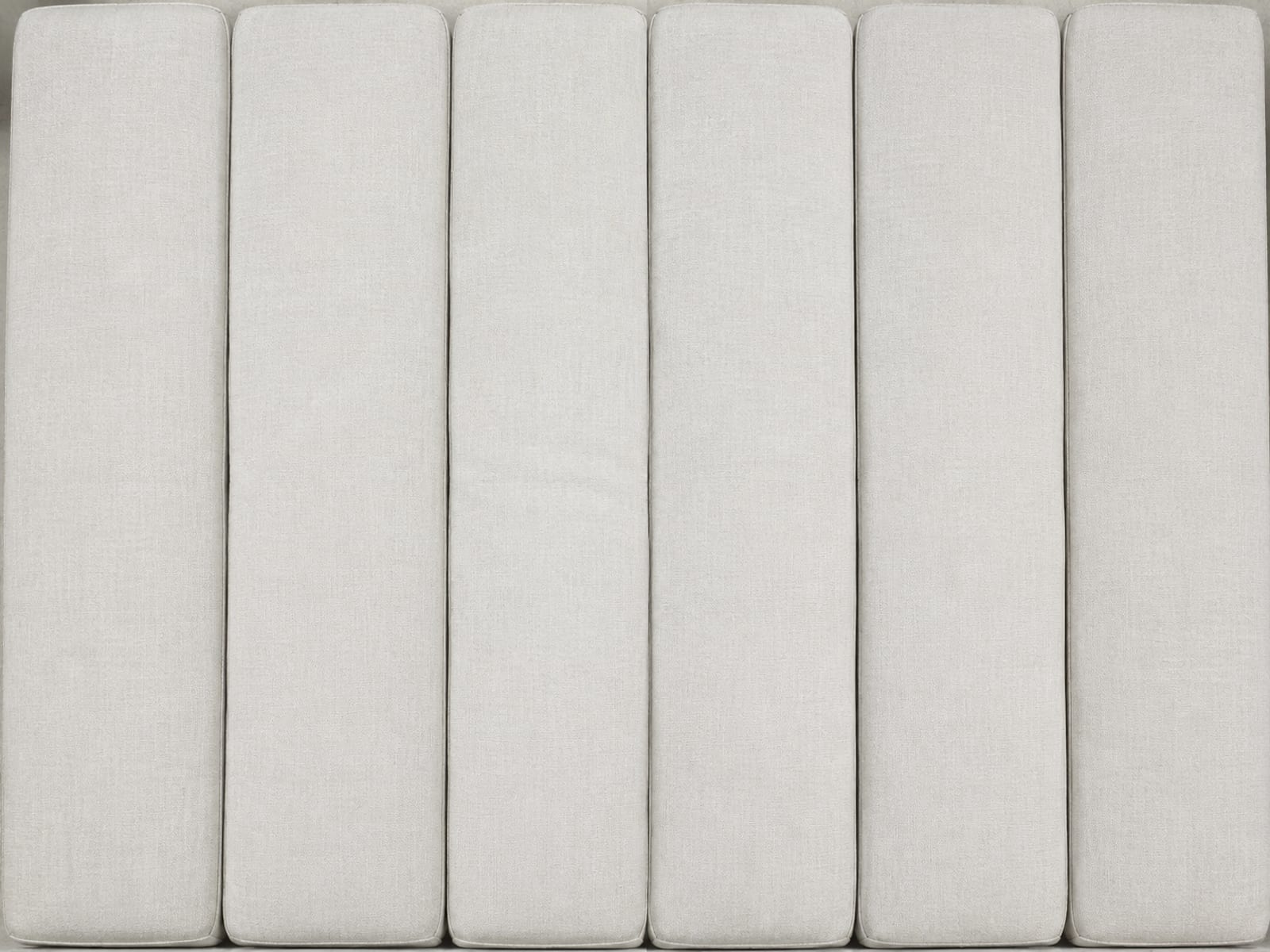 The seat line of a long six-seat sofa cropped tight, six cushions and the five seams dividing them filling the frame from edge to edge
