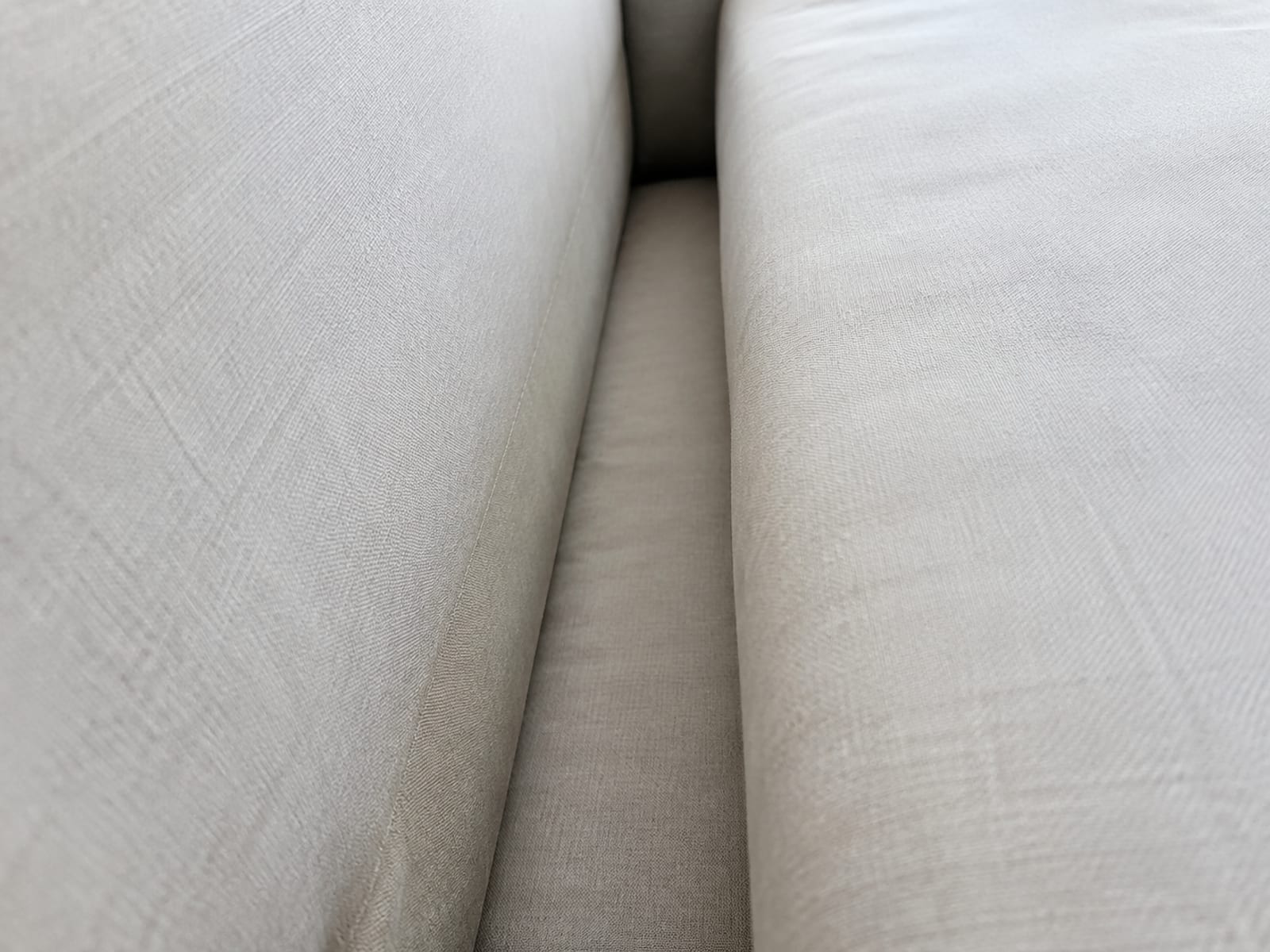 A close view down into the open crevice between a seat cushion and the back cushion, the channel running clear and deep to the woven platform below