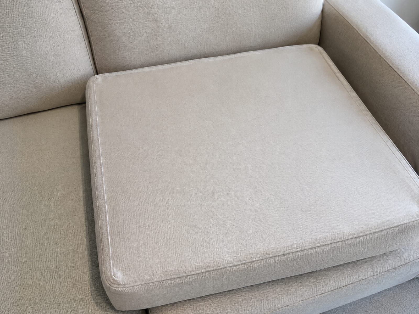 One seat cushion turned over on the sofa so its plain unfinished underside faces up, the seam running around its edge