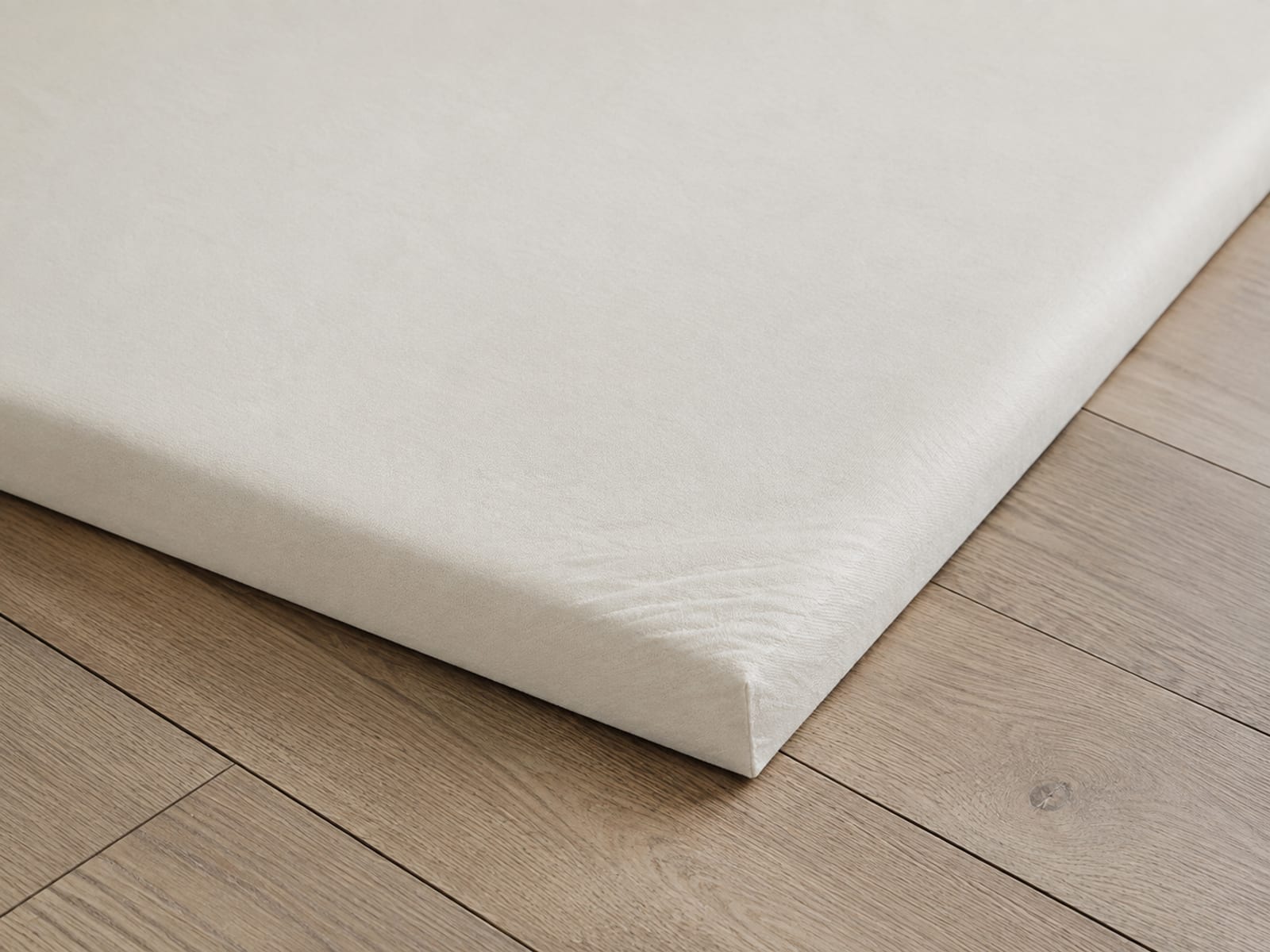 Two strips of the same plain woven upholstery cloth laid side by side on a pale wooden surface, identical in weave and width, one noticeably paler in tone