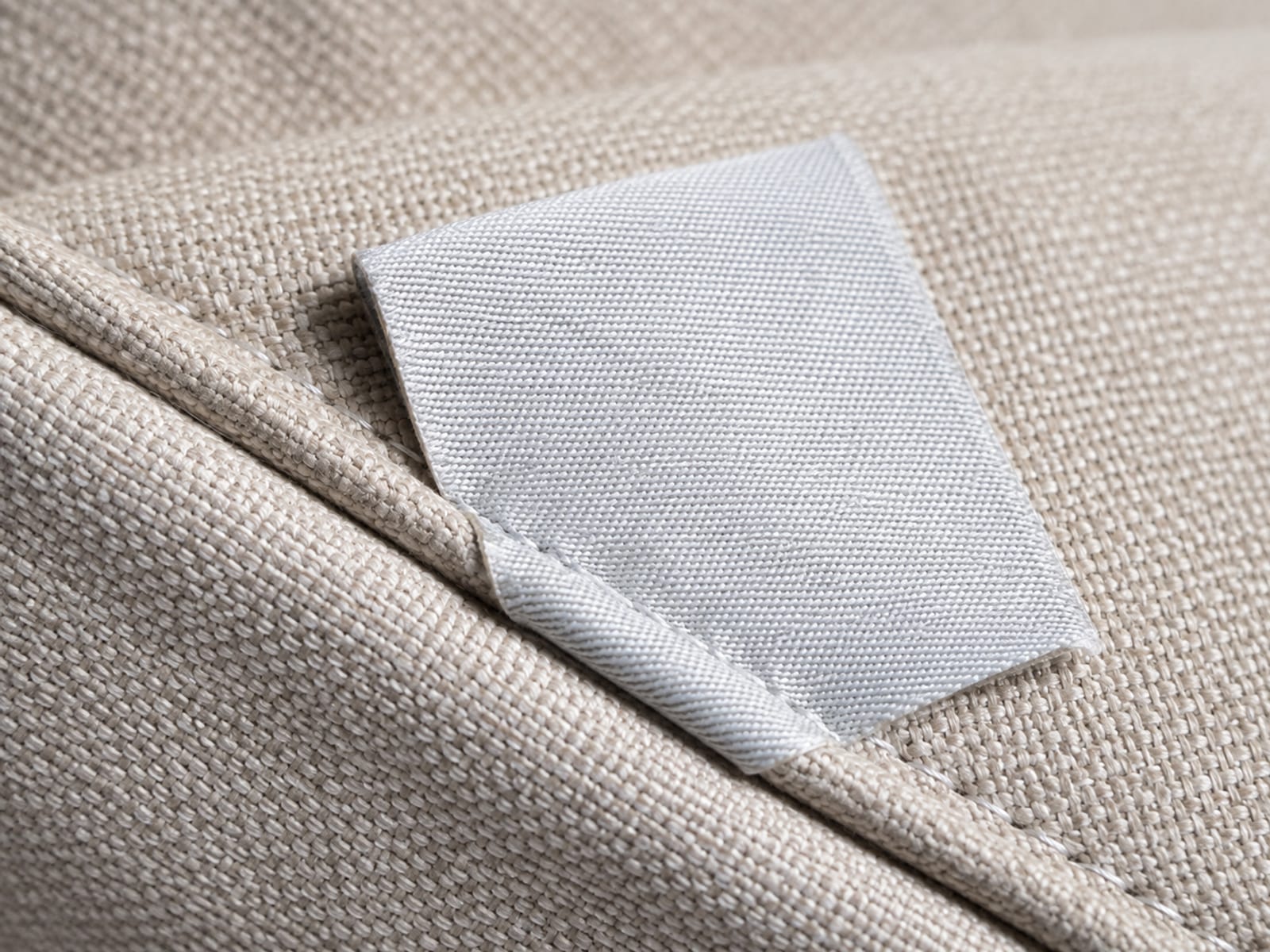 A small pale fabric care label stitched into the piped seam on the underside of a seat cushion