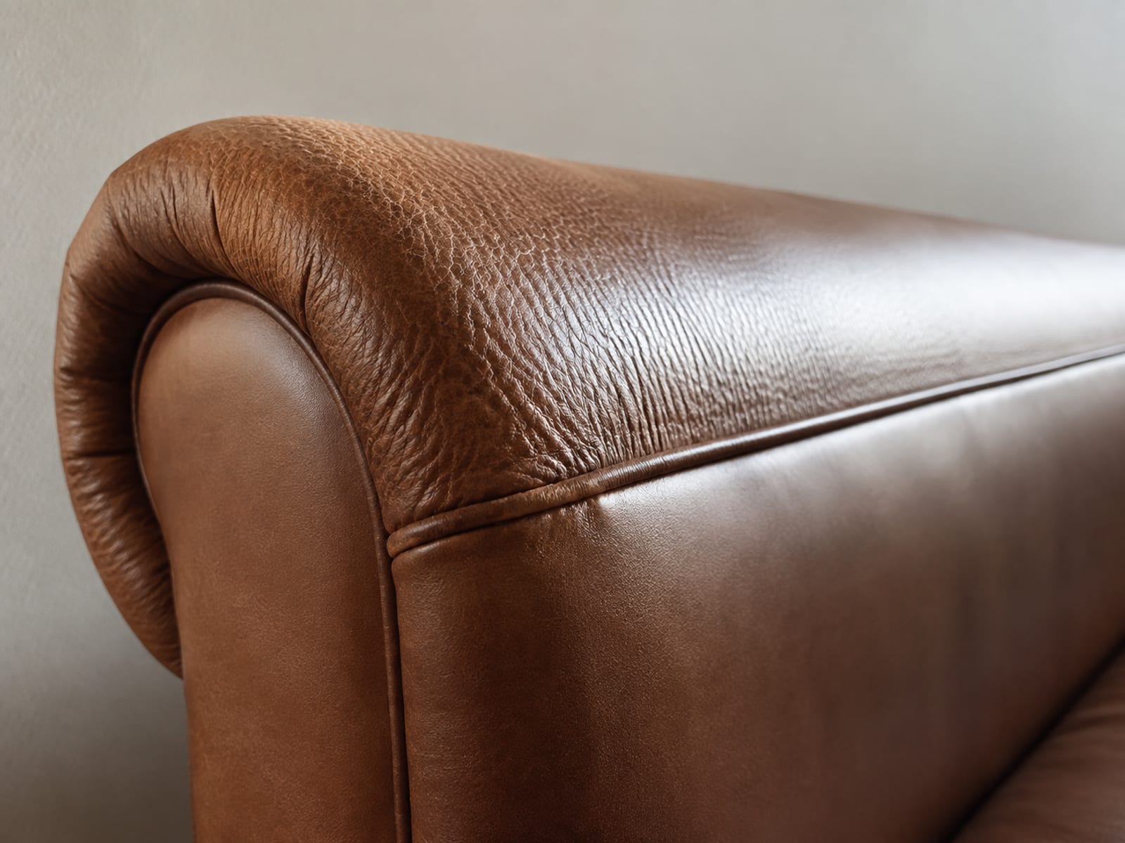 The arm of a leather sofa, softly creased leather over the top roll meeting smooth taut leather on the flat side panel below