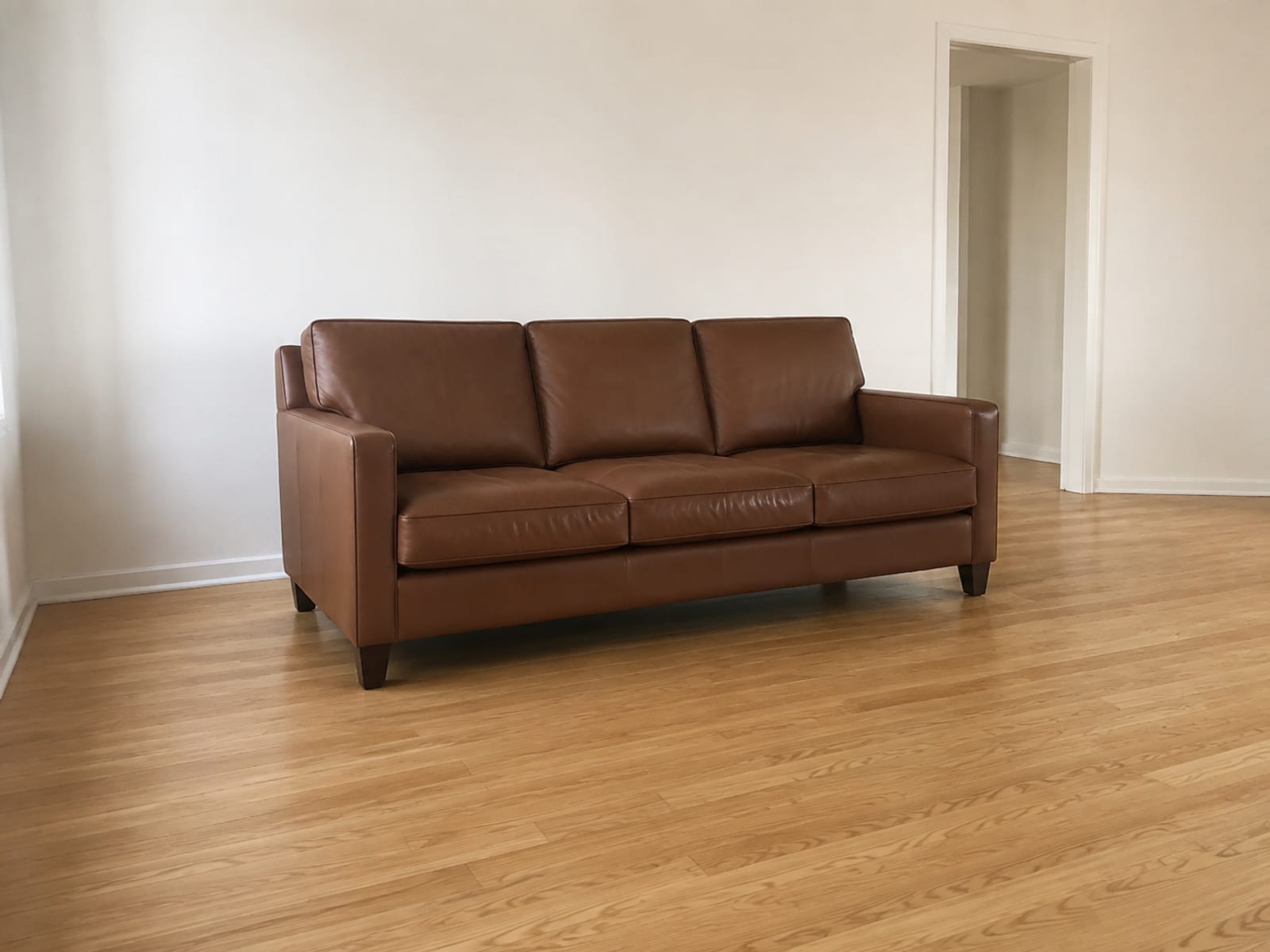 A mid-brown leather three-seat sofa alone in an empty room with nothing at all on its seat or arms