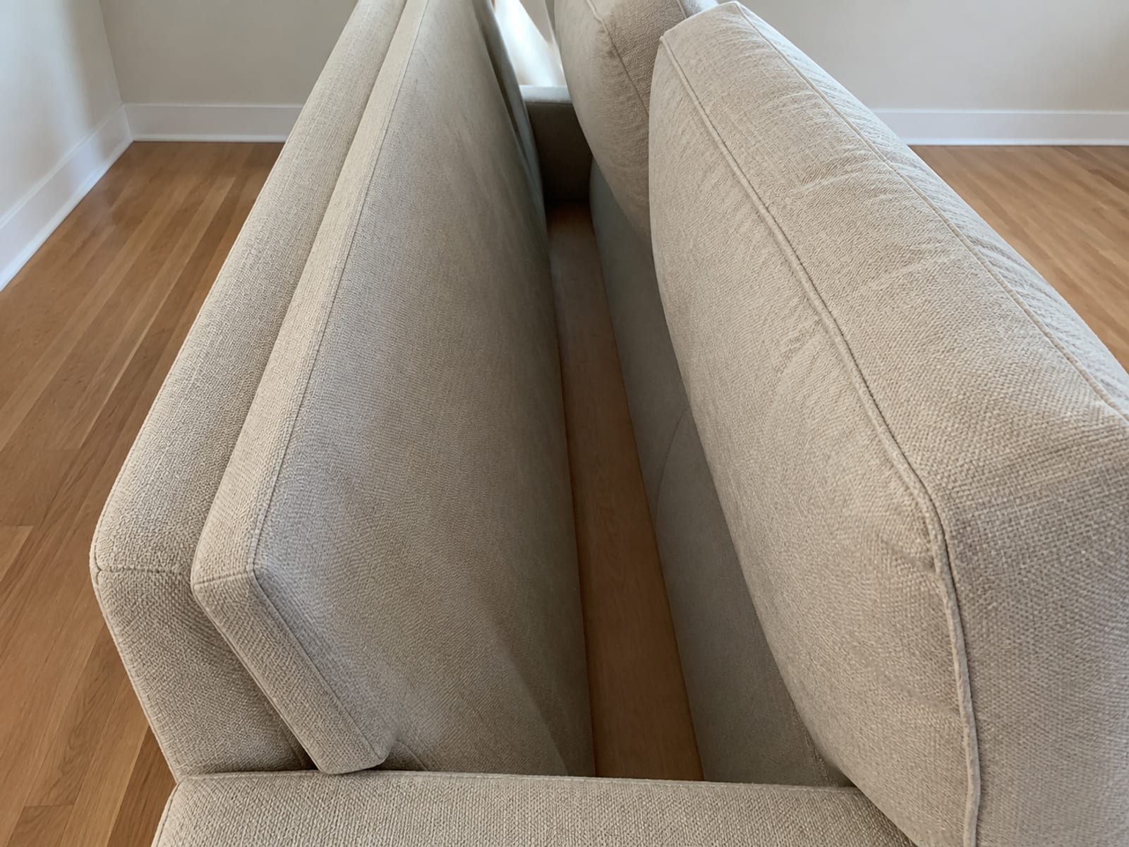 The back cushions of a sofa tipped forward, opening the narrow upright channel behind them down to the frame rail