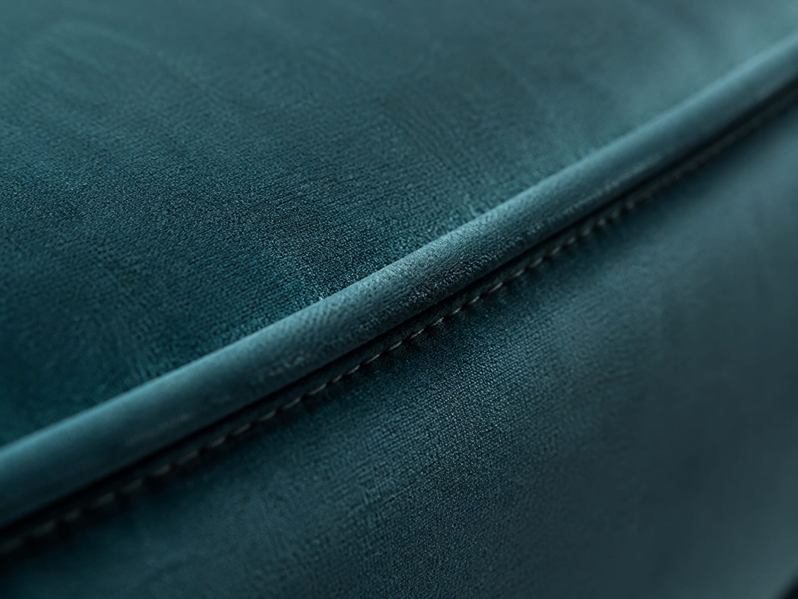 An extremely close view along a stitched piped seam where a velvet cushion meets its side panel, pile rising on both sides