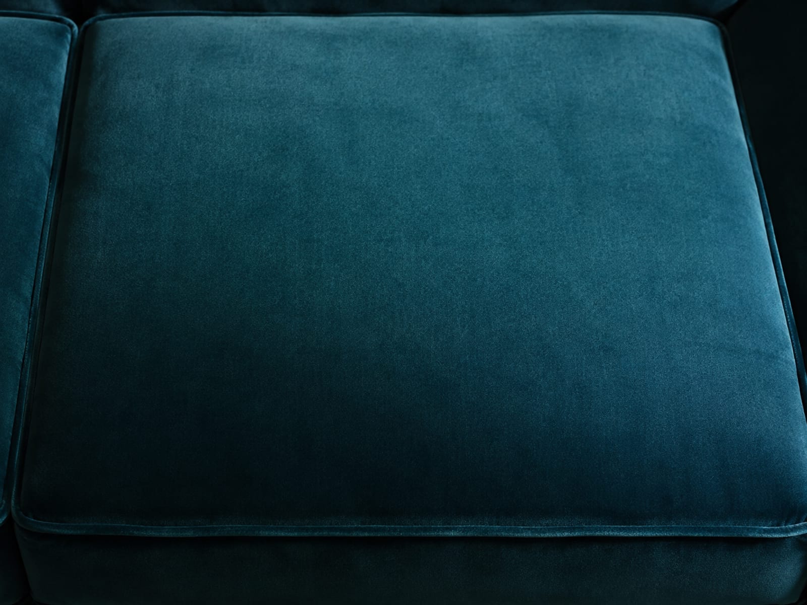 A single deep teal velvet cushion filling the frame, its near half reading darker than its far half across a soft gradual transition