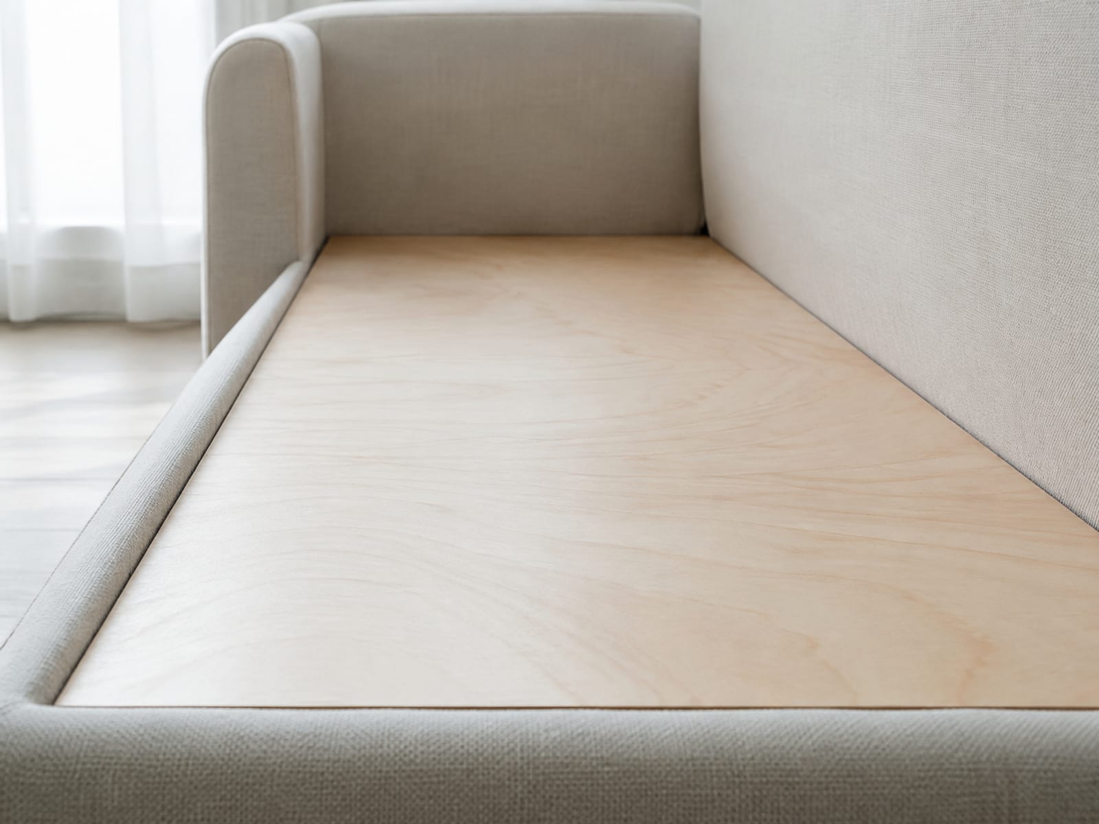 A flat pale timber panel lying across the open seat platform of a sofa with the cushions absent, spanning the frame from front rail to back
