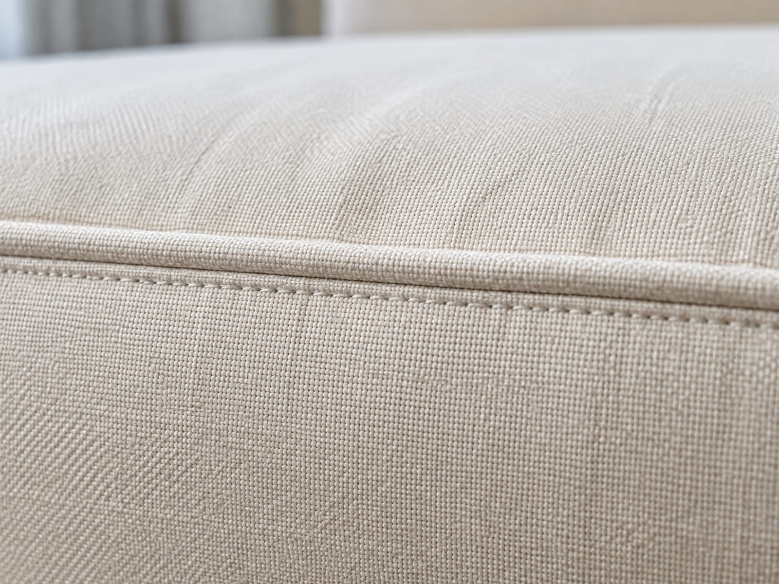 An extremely close view along the piped seam at the corner of a seat cushion, the stitch line running unbroken with no zip, pull or opening anywhere