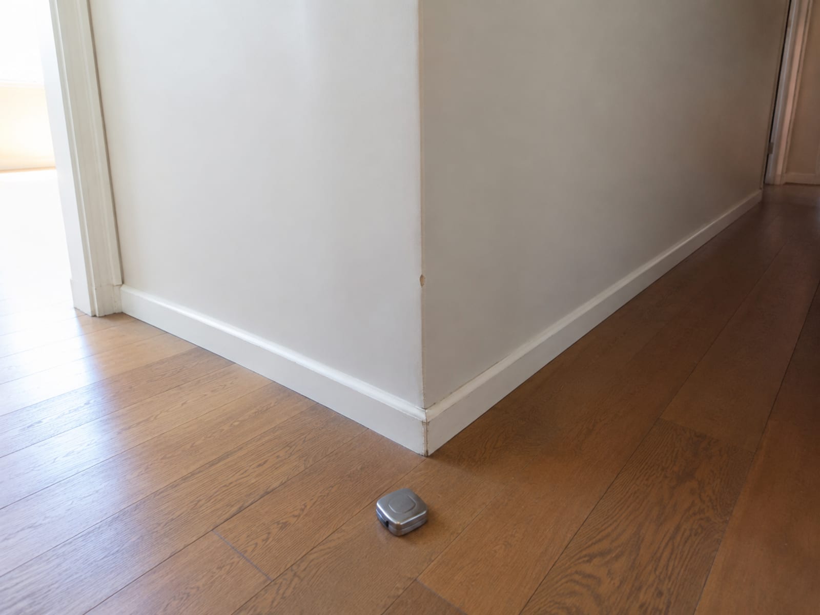 A narrow empty hallway turning ninety degrees, both legs of the turn visible, with a coiled tape measure set down on the floor at the corner