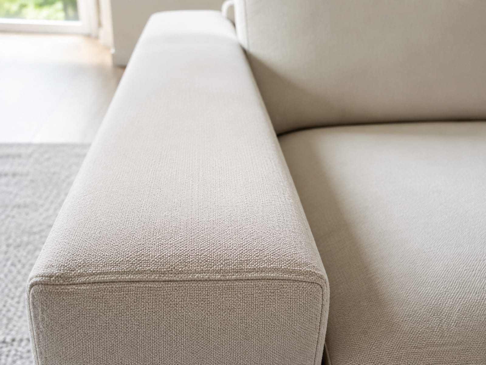 A close view along the flat upholstered top of a sofa arm at seat height, running away from the camera into soft focus beside the seat cushion