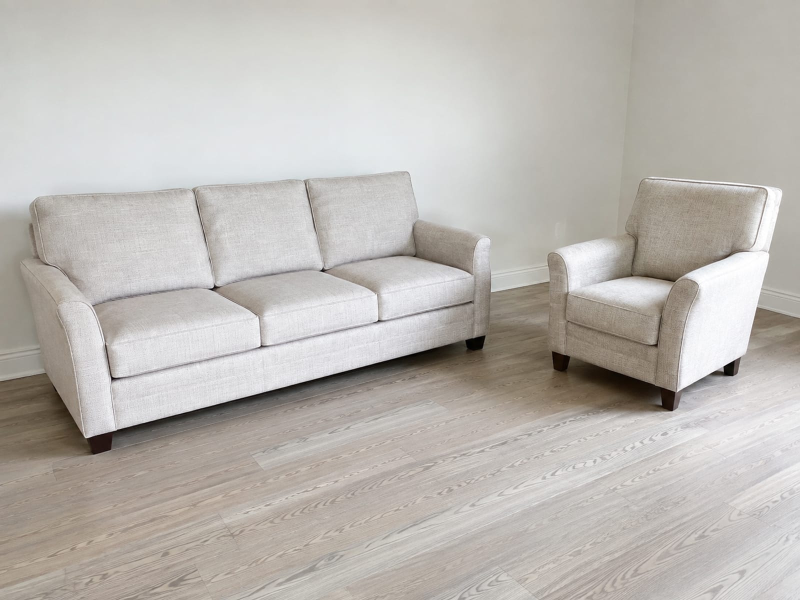 A three-seat sofa and a single upholstered armchair in the same pale fabric standing at an angle to one another in an otherwise bare room