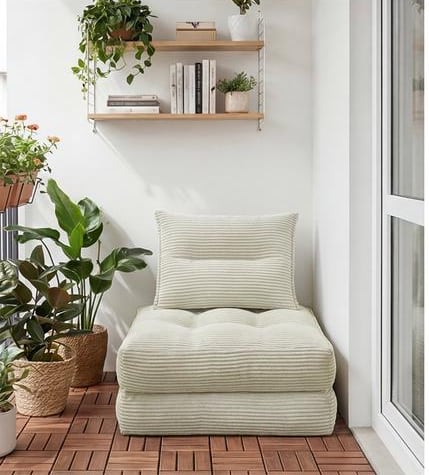 The same style of convertible folded upright as a chair, its back cushion in place, in a bright corner beside potted plants