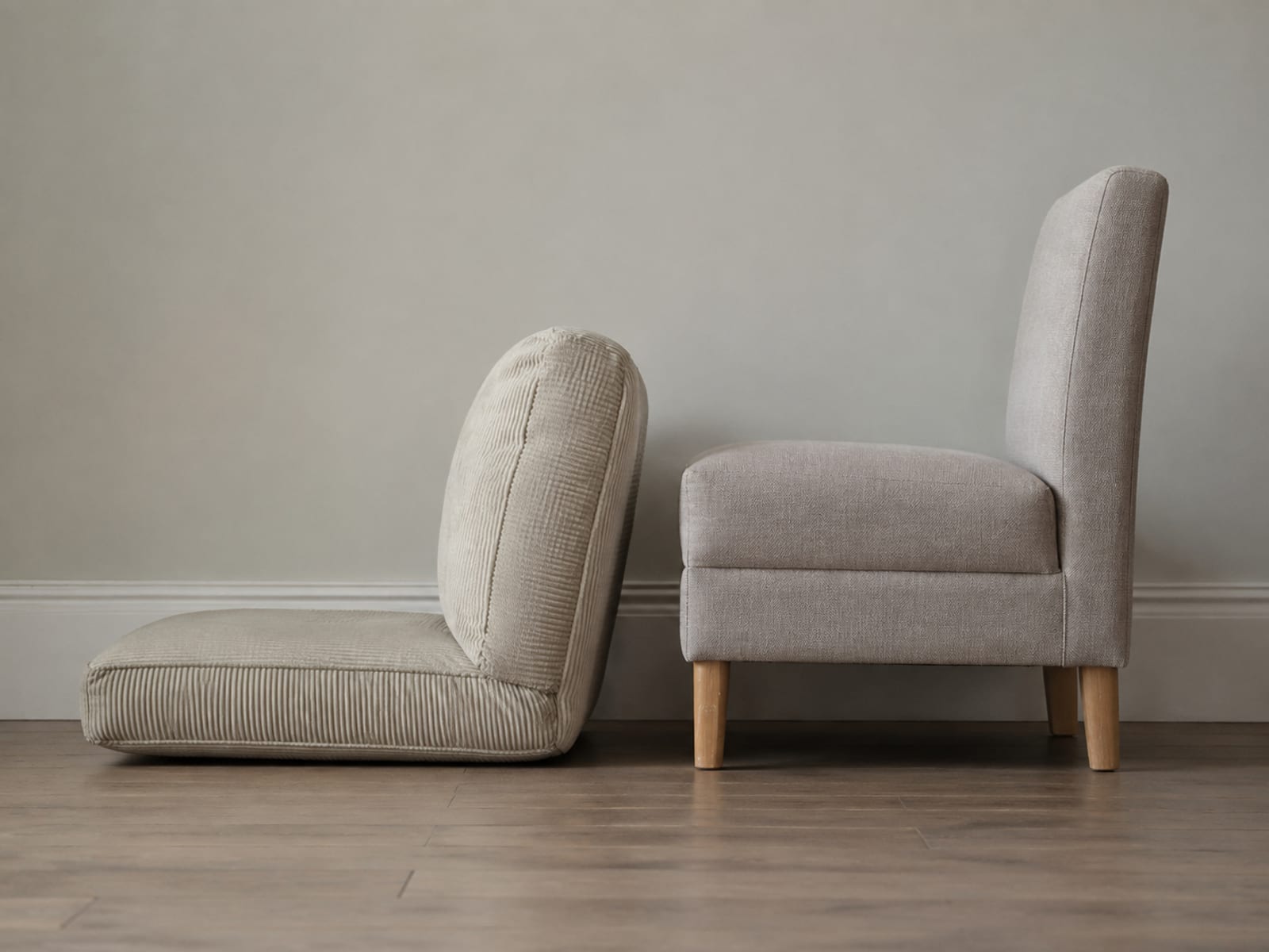 A low floor-level convertible seat and a normal upholstered bedroom chair side by side against one wall, seen from the side so the difference in seat height is visible