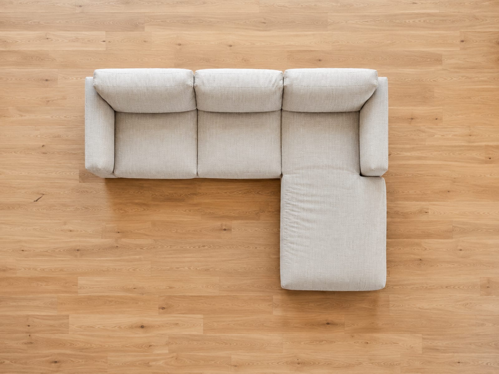 A sofa with a chaise seen from directly overhead so its L-shaped footprint reads flat against the floorboards