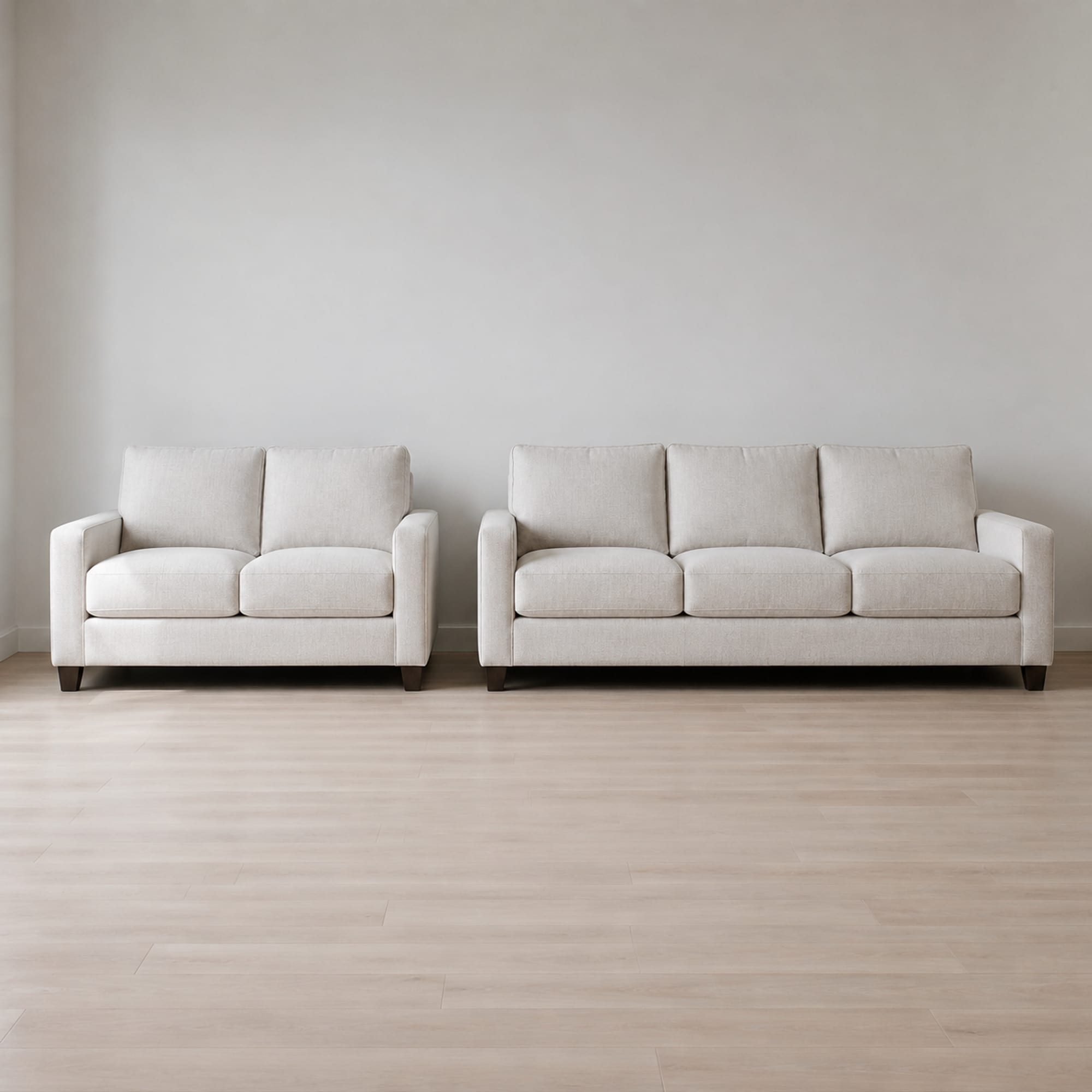 A two-seat loveseat and a three-seat sofa of the same design and the same pale weave standing side by side against one wall, identical in depth, height, arms and cushions
