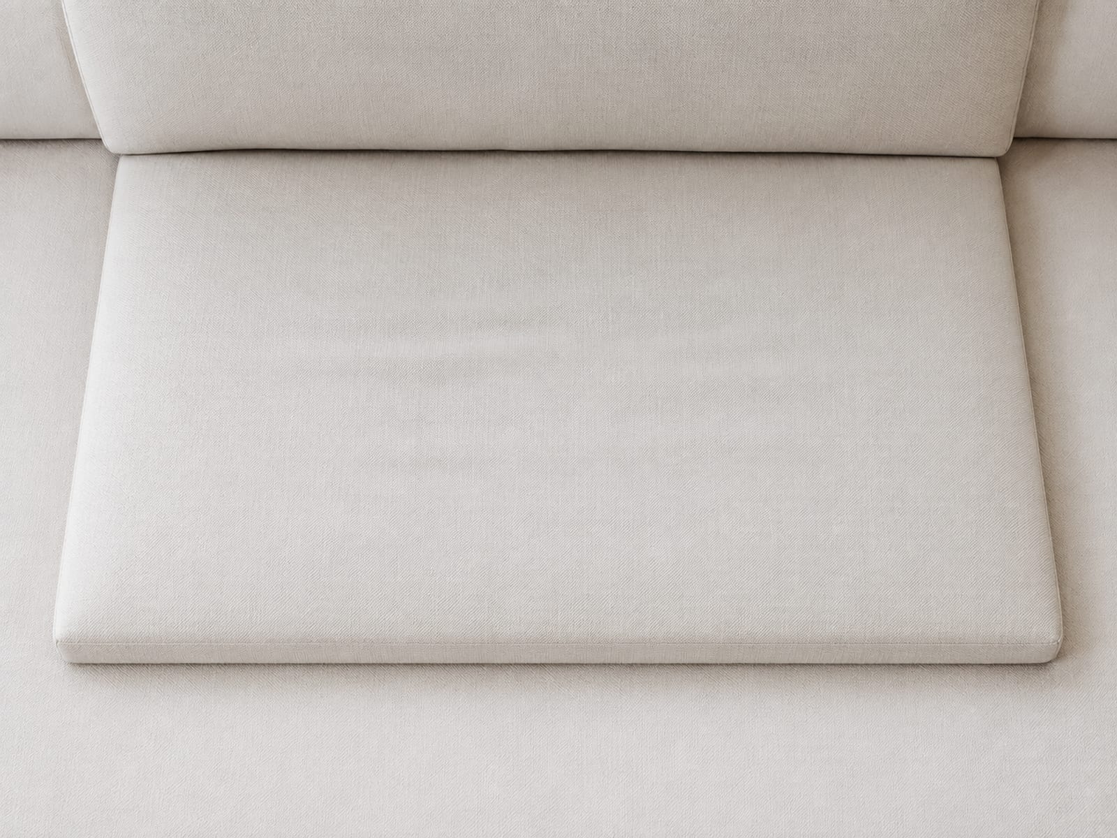 A close view straight down onto a single sofa seat cushion whose front-to-back reach is visibly short, running from the front edge to the base of the back cushion