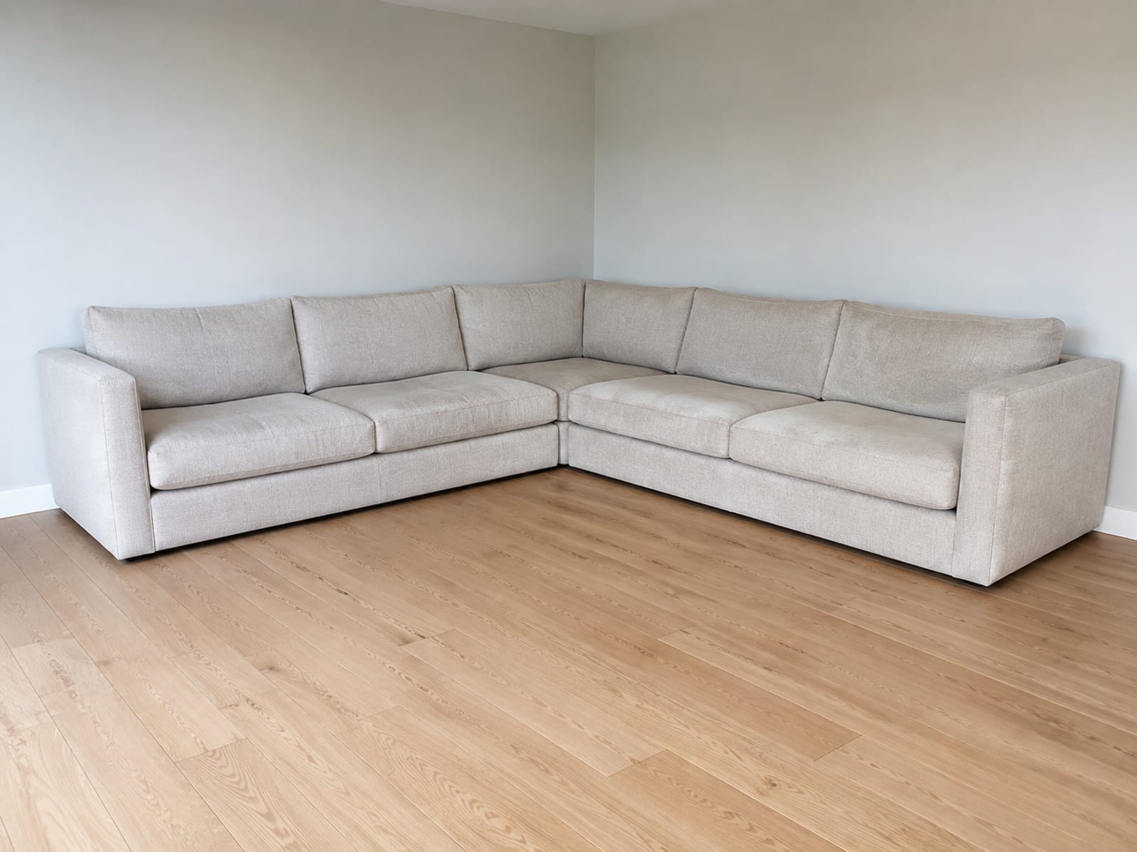 A sectional filling the corner of a bare room so both walls it occupies read at once, with the remaining open floor in the foreground