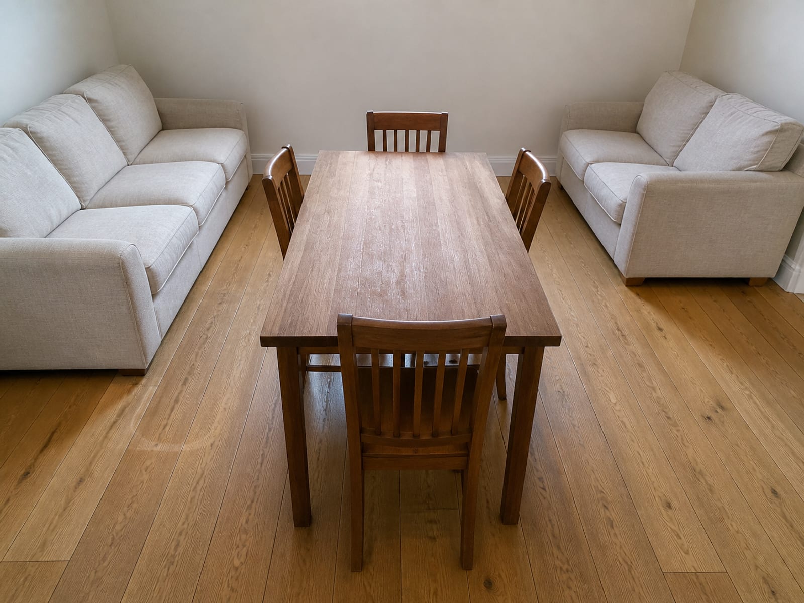 Two seating pieces pushed back against opposite walls with a plain dining table and chairs set up in the cleared space between them