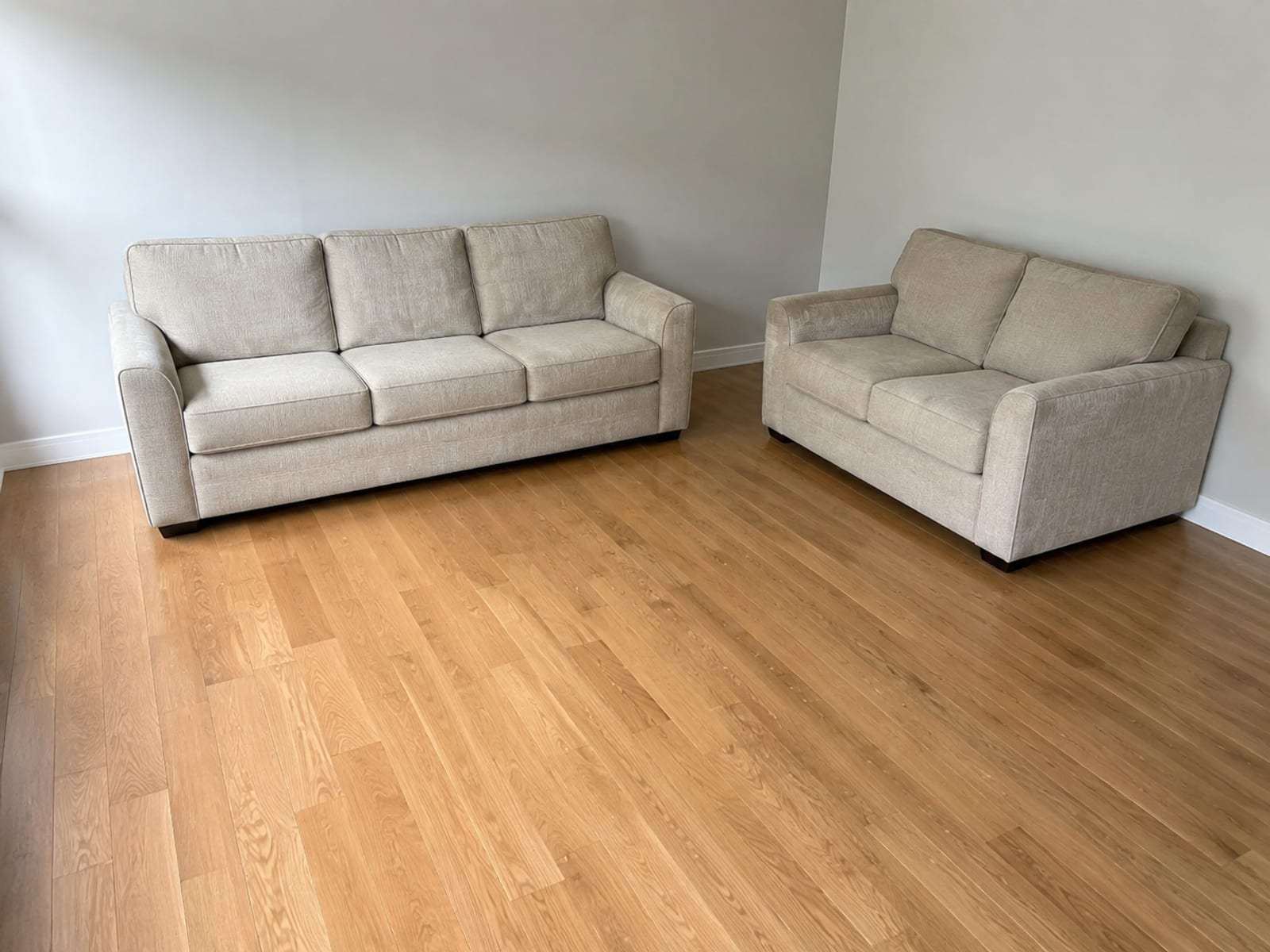 A three-seat sofa against one wall and a loveseat against the adjacent wall at right angles, with open floor between them