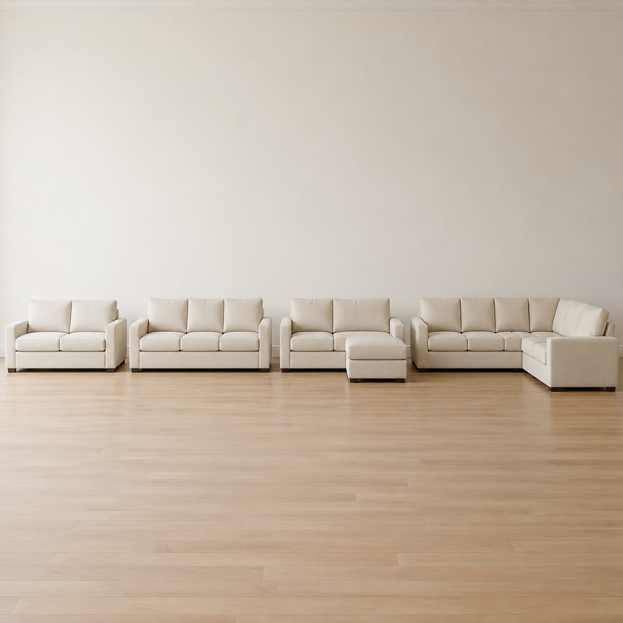 Four pieces of seating in one identical pale oatmeal upholstery standing in a row along a wall, stepping up in size from a loveseat to an L-shaped sectional