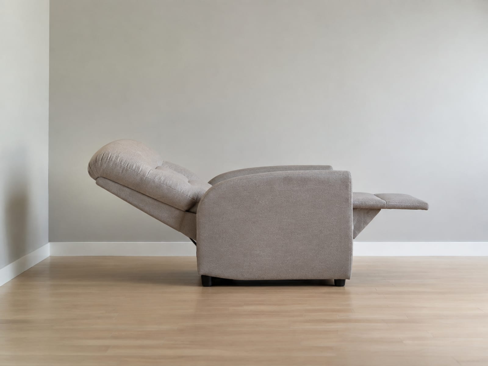 A single upholstered reclining chair fully reclined with its footrest up, standing away from a plain wall so the clear gap between the top of its back and the wall reads as the subject