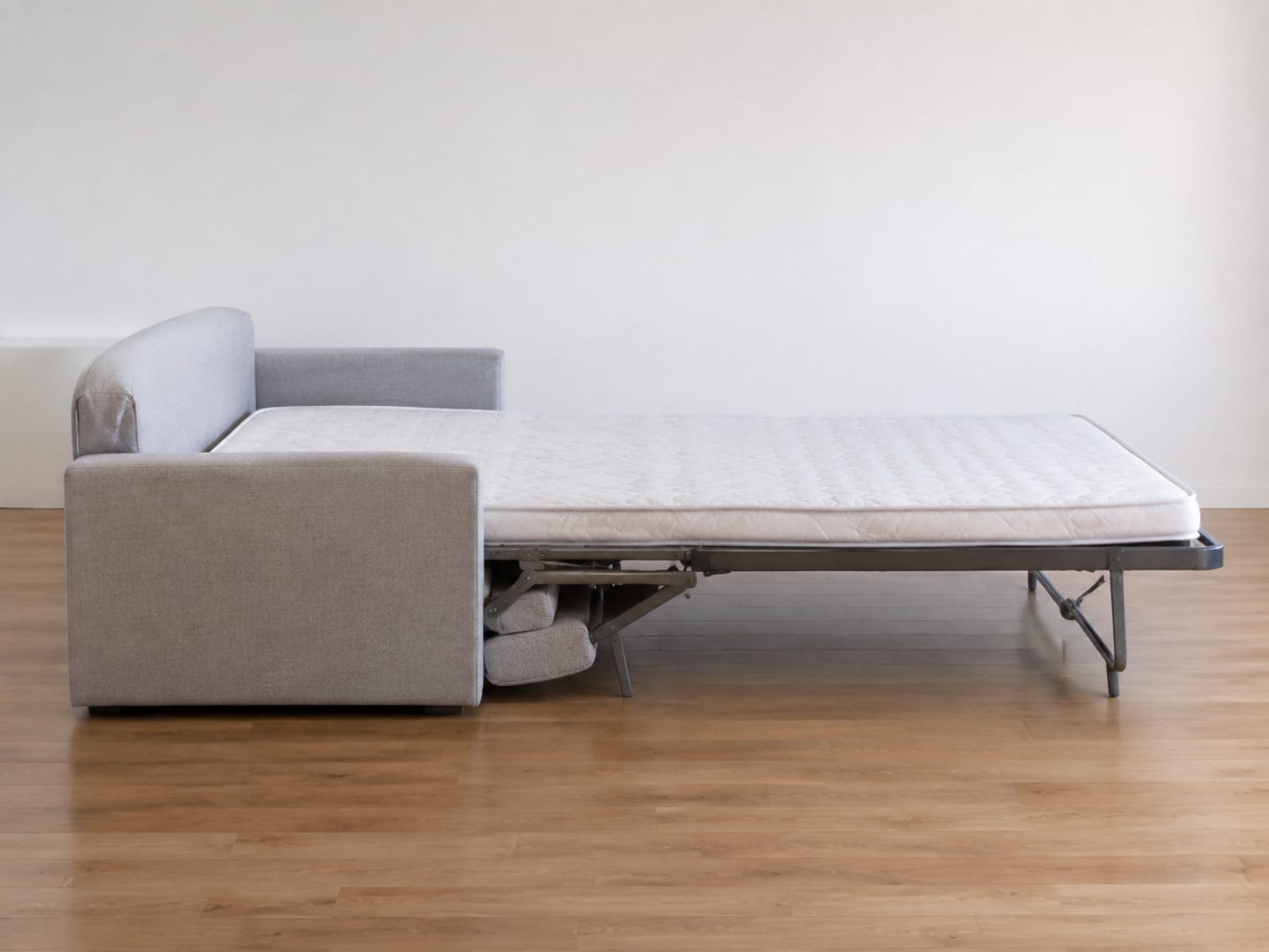 A sleeper sofa opened flat into its bed position in an empty room, seen square from the side with bare floor visible beyond its far edge