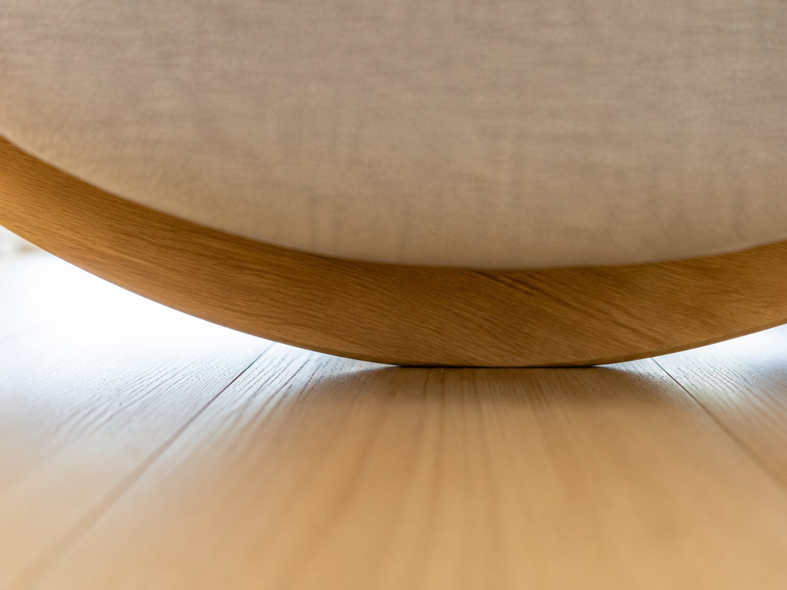 An extremely close view at floor level of the curved wooden runner beneath an armchair where it meets bare oak floorboards