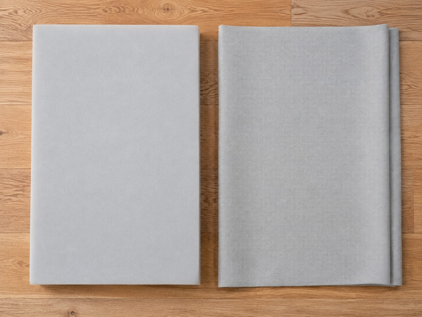 A plain pale gray block of upholstery foam and a loose woven cover lying flat side by side on bare floorboards, seen square from directly above
