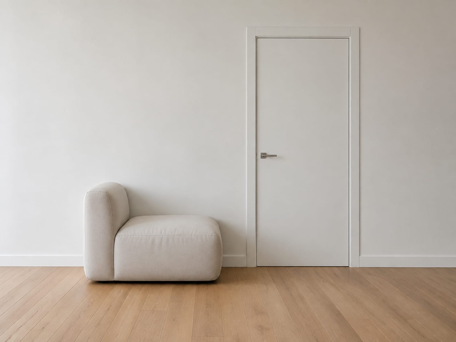A boneless sofa standing beside a closed interior door in a bare room, seen from the side, with the top of the seat far below the door handle