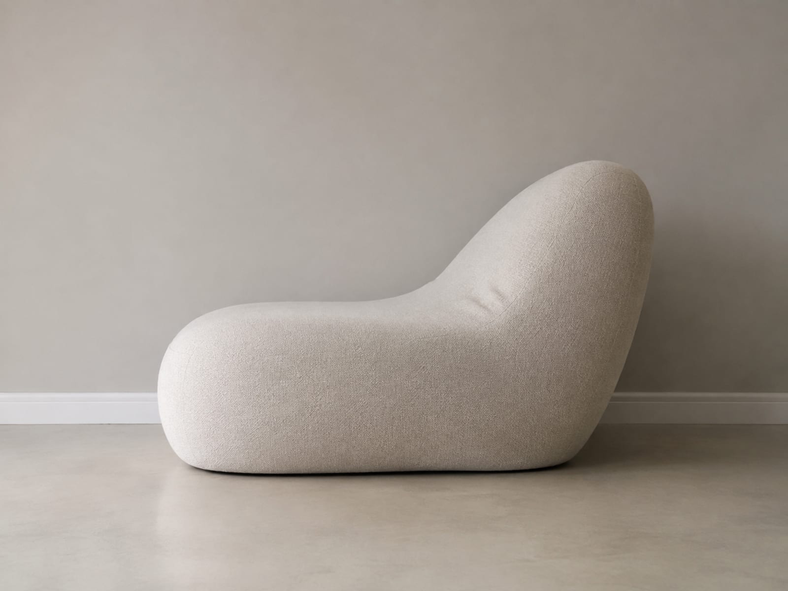 A boneless sofa seen square from the side against a plain wall, its back leaning away in one continuous curve with no straight edge anywhere, above a level baseboard