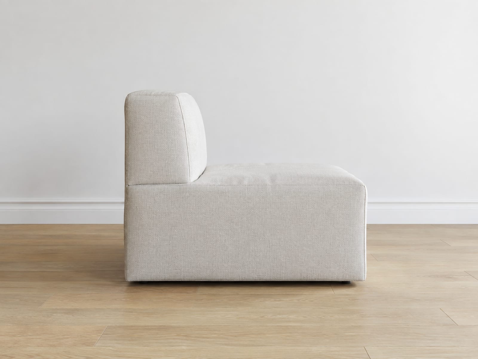 A single armless seat module standing alone on bare oak floorboards in an empty room, seen square from the side at seat height, with an ordinary seat depth and an upright back