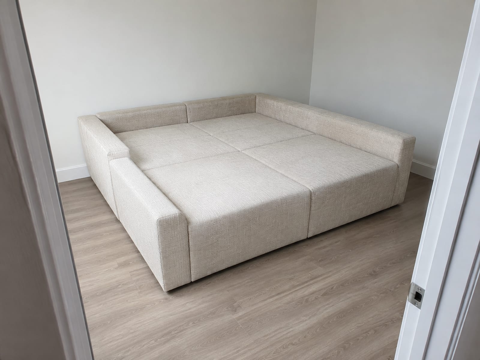 A closed pit-style sectional occupying most of a small bare room, seen from the doorway with the door frame edging the picture and narrow bands of floor left on every side