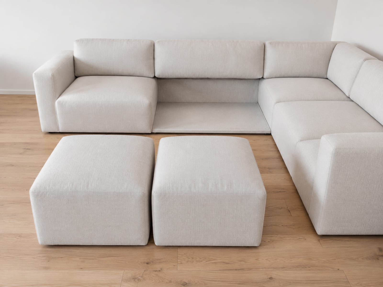 Two matching upholstered ottomans standing side by side on bare floorboards away from a sectional, with the open gap they came from visible behind them