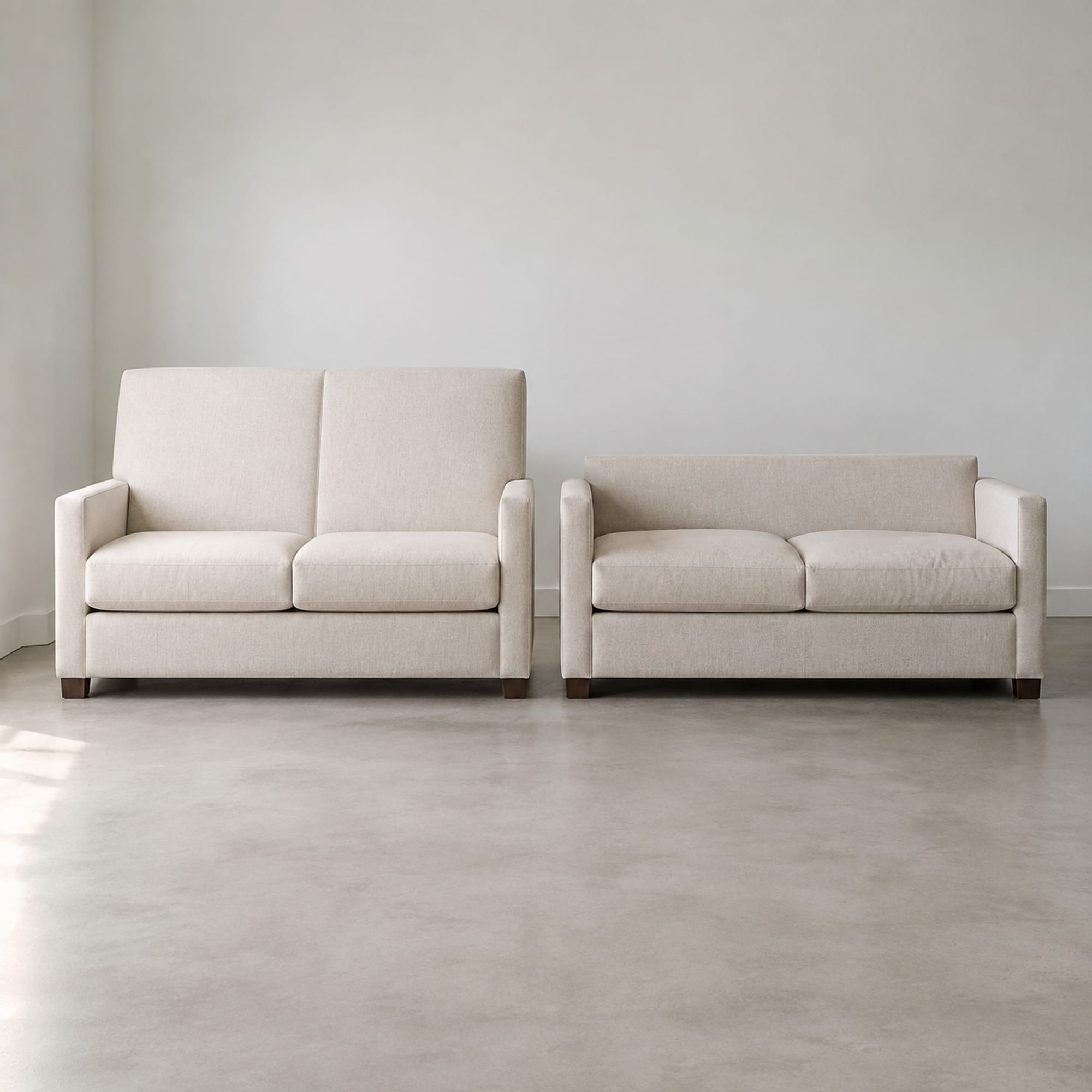 Two sofas in the same pale oatmeal weave standing side by side against one wall, the left with a tall upright back and the right with a lower back over a deeper seat