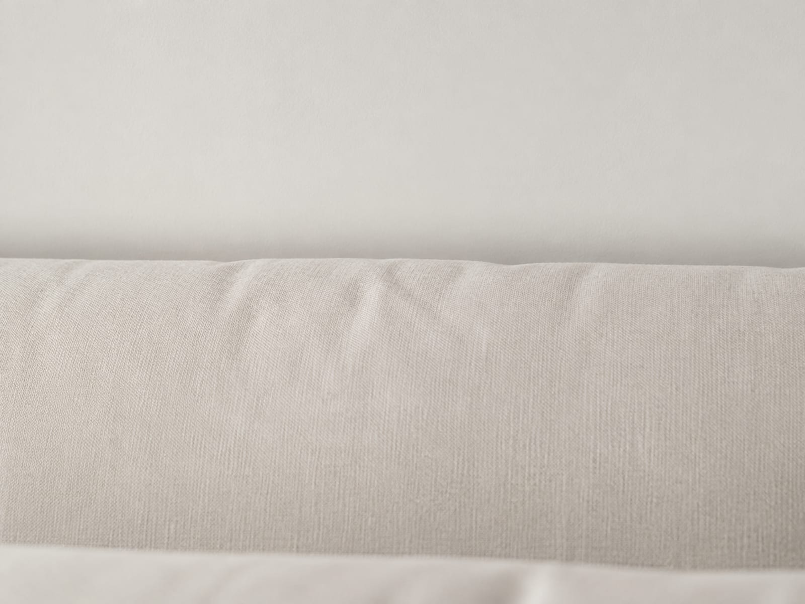 A close side view of the top edge of a sofa back cushion against a plain wall, with a band of empty wall above it showing where the support stops